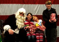 Santa Claus hands presents to Victoria Haltli, Alyssa Haltli, and Raiff Haltli during the 419th Fighter Wing’s holiday party. (U.S. Air Force photo /Senior Airman Allen Stokes)