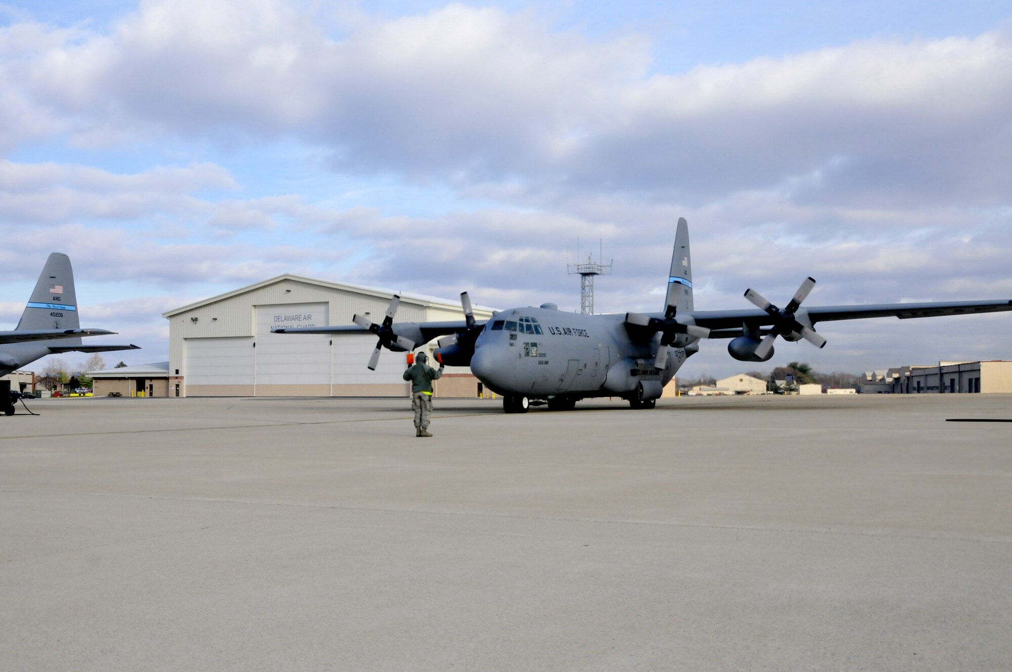 A crew chief marshals in Delaware Air National Guard C-130 tail #40210 at the New Castle ANG Base, Del. on Dec. 7, 2013 after the 13 aircrew members completed a Joint Precision Airdrop System training mission. At left is C-130 tail #40206, which just landed after the seven aircrew members completed a local proficiency training mission. The two missions are recognized by the Delaware ANG to help celebrate the 166th Airlift Wing’s reaching the milestone of 175,000 safe flying hours without a serious mishap over the last 50 years. (U.S. Air National Guard photo by Tech. Sgt. Benjamin Matwey)