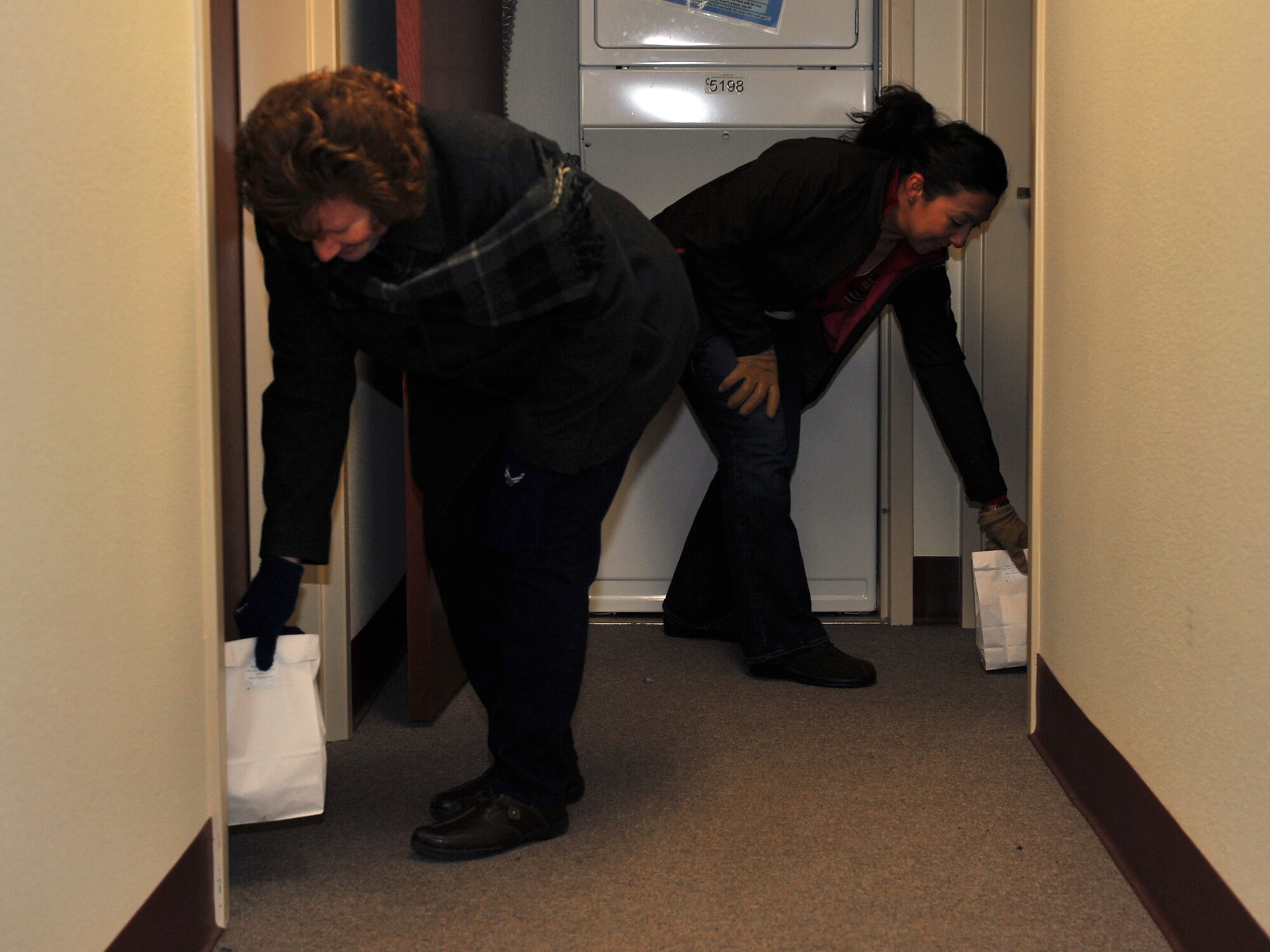 Jill Newberry and Bernadette Hervas, Officer Spouses Club members, leave bags of cookies in front of dorm rooms as part of the cookie drive Dec. 9, 2013, at Fairchild Air Force Base, Wash. The cookie drive is an annual event hosted by the Officers’ Spouses Club with help from the chapel staff and the Lilac Princesses. (U.S. Air Force photo by Staff Sgt. Veronica Montes/Released)