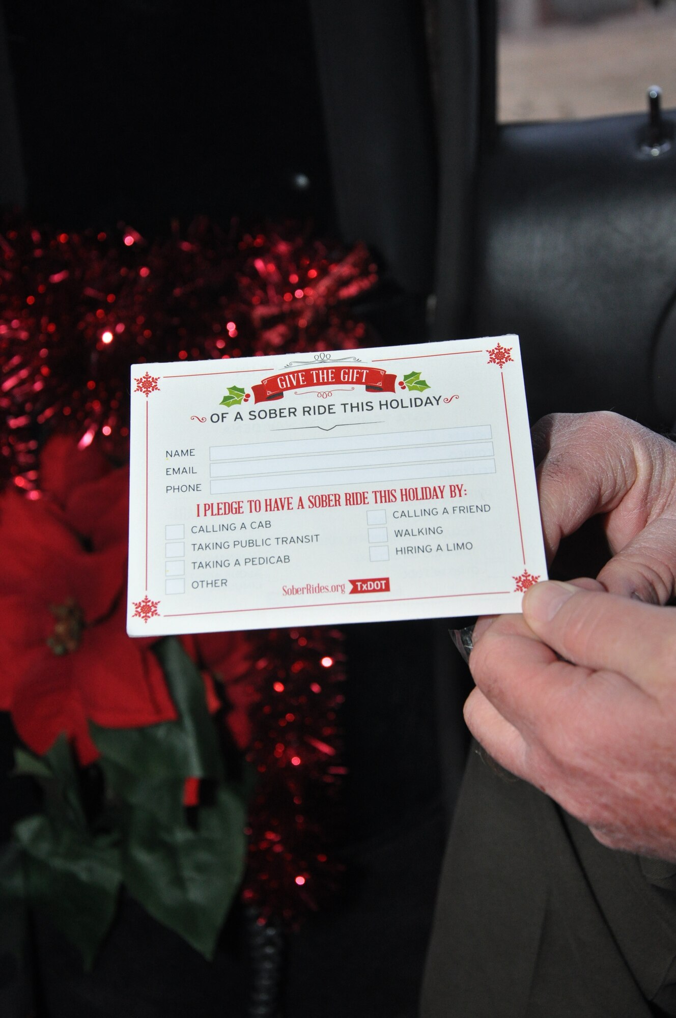 GOODFELLOW AIR FORCE BASE, Texas -- Todd Deere, Texas Department of Transportation safety representative holds a pledge card in the Sober Sleigh outside the base theater Dec. 5. Deere and other volunteers handed out the pledge cards. The cards list choices that party goers have to get home safely, such as calling a cab or walking home. (U.S. Air Force photo/ Airman 1st Class Breonna Veal)