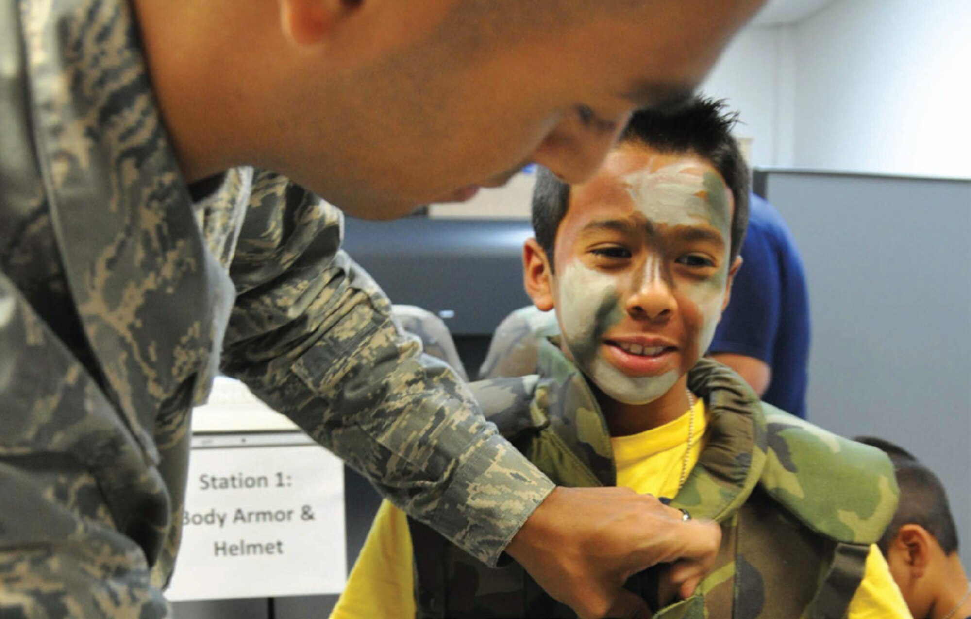 Senior Airman Jonathan Villa Vargas, 452nd Logistics Readiness Squadron, fits 10-year-old Cristian Medina, with Individual Body Armor during a mock deployment line set up for kids at the first-ever Operation Family First event held in Building 385, July 13. Medina was one of about 40 kids who participated along with parents and other relatives. The event was designed to give children a feel for what their deploying parents go through during a real-world deployment. (U.S. Air Force photo/Staff Sgt. Joe Davidson)