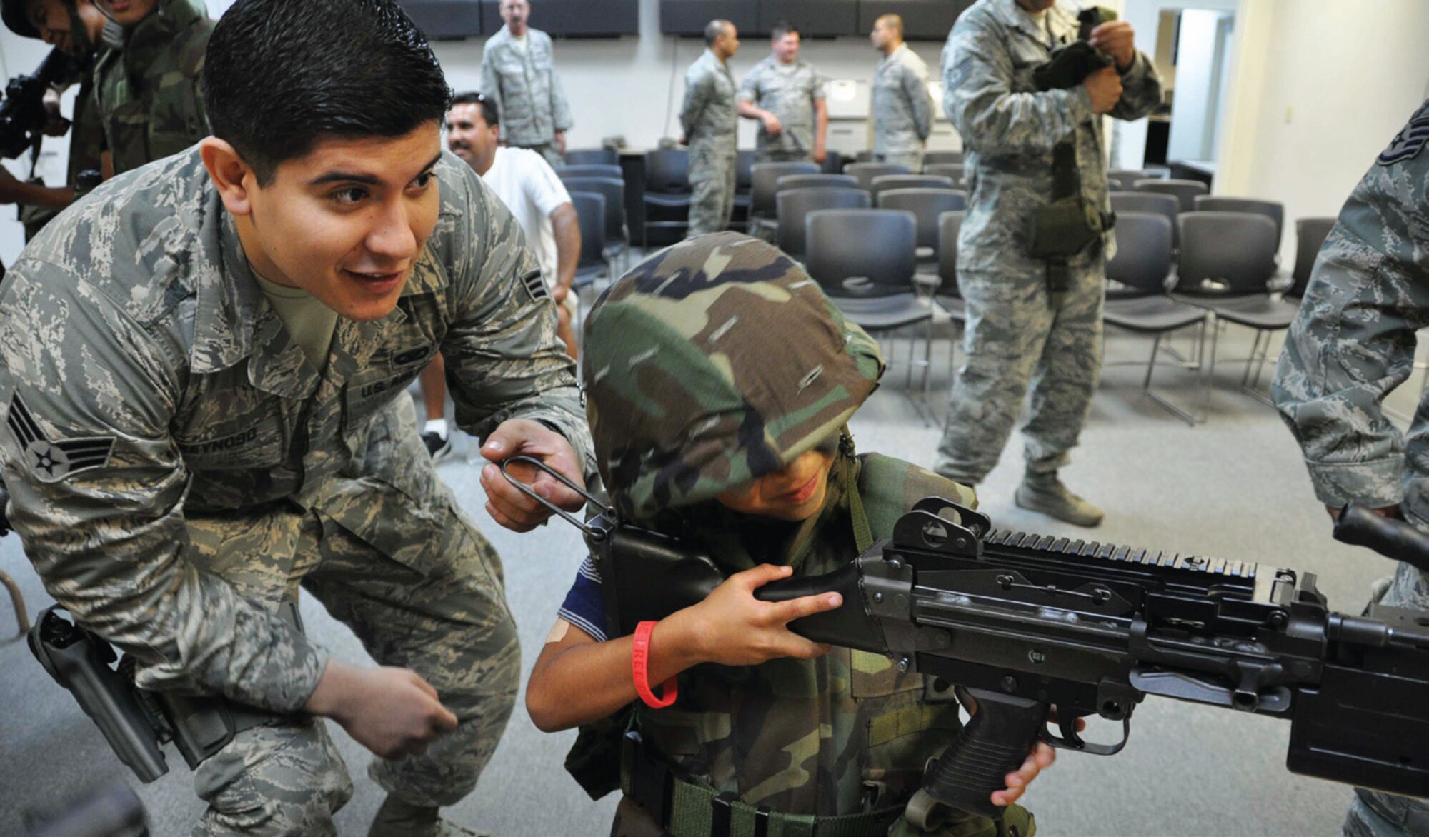 Senior Airman Andrew Reynoso, 452nd Security Forces Squadron, helps six-year-old Giovanni Medina get a clear sight picture as he holds on tight to the M240-Bravo Machine Gun. This, as well as other weapons, was on display during the Logistics Readiness Squadron’s Operation Family First event held in Building 385, July 13. (U.S. Air Force photo/Staff Sgt. Joe Davidson)