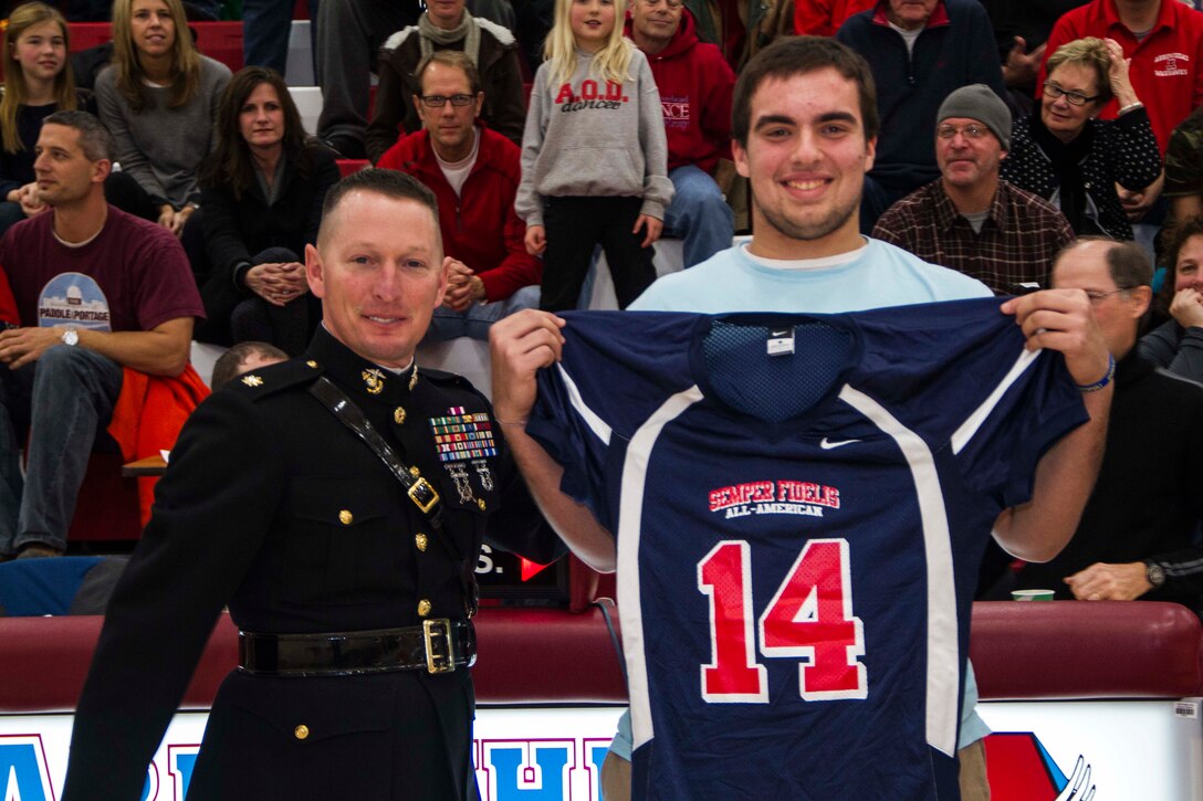 Maj. Charles D. Godwin, Recruiting Station Milwaukee Commanding Officer, presents a Semper Fidelis All-American Bowl jersey to Arrowhead High School senior George Panos during a basketball game in Hartland, Wis., Dec. 6, 2013. Panos will represent the state of Wisconsin in the Semper Fidelis All-American Bowl in January in Carlson, Calif. Panos plays offensive line and is committed to the University of Wisconsin-Madison.
