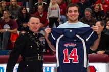 Maj. Charles D. Godwin, Recruiting Station Milwaukee Commanding Officer, presents a Semper Fidelis All-American Bowl jersey to Arrowhead High School senior George Panos during a basketball game in Hartland, Wis., Dec. 6, 2013. Panos will represent the state of Wisconsin in the Semper Fidelis All-American Bowl in January in Carlson, Calif. Panos plays offensive line and is committed to the University of Wisconsin-Madison.