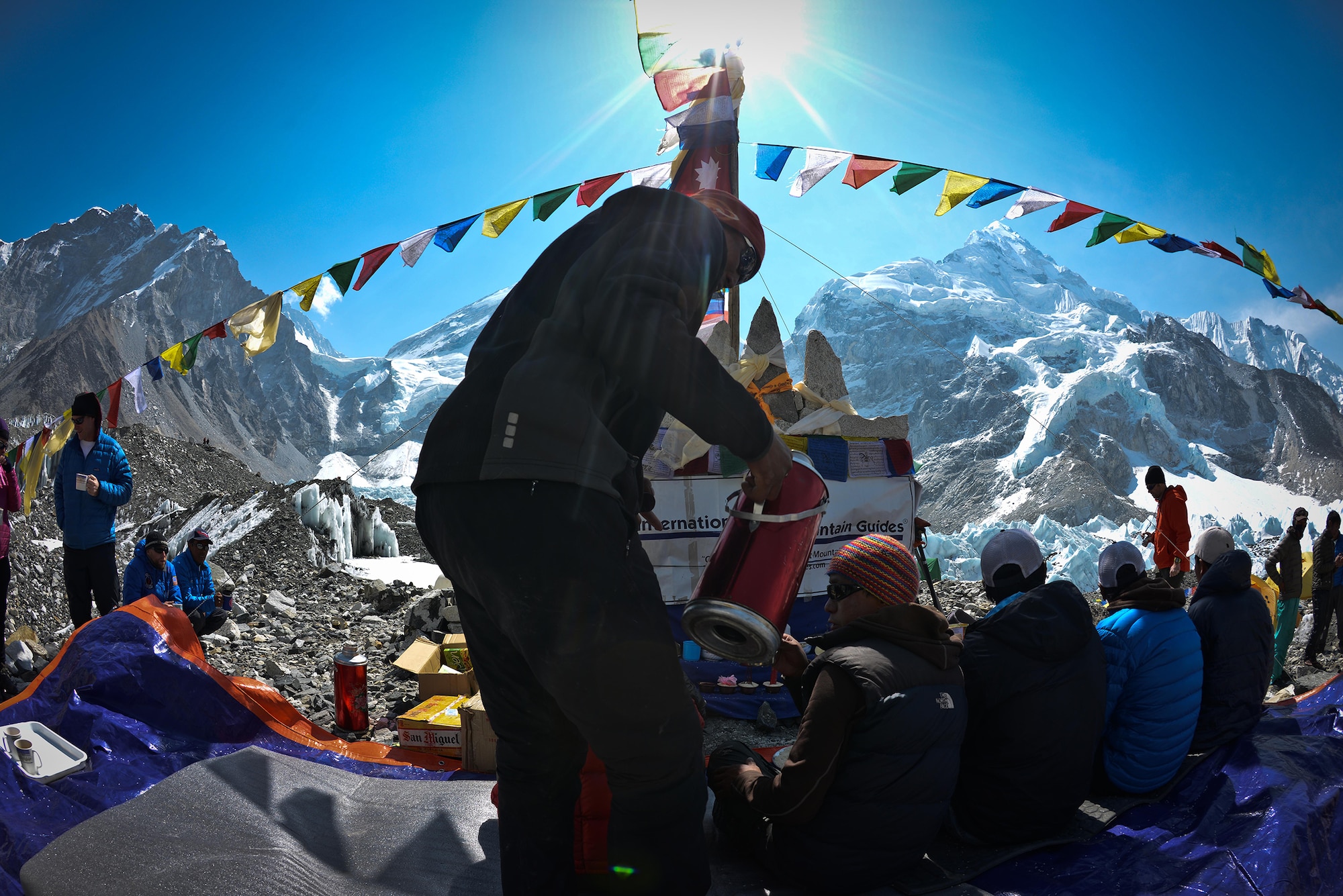 Dawa fills the teacups of the praying Sherpa as they are performing the Puja, a ceremony to bless the climbers, both Sherpa and non-Shepra, and their equipment April 15, 2013. The Sherpa are lined up and chant a soothing, soulful string of prayers to ask for blessing of the climb. Behind Dawa is Everest; the peak to the right is Nuptse. (photo by Nick Gibson)  