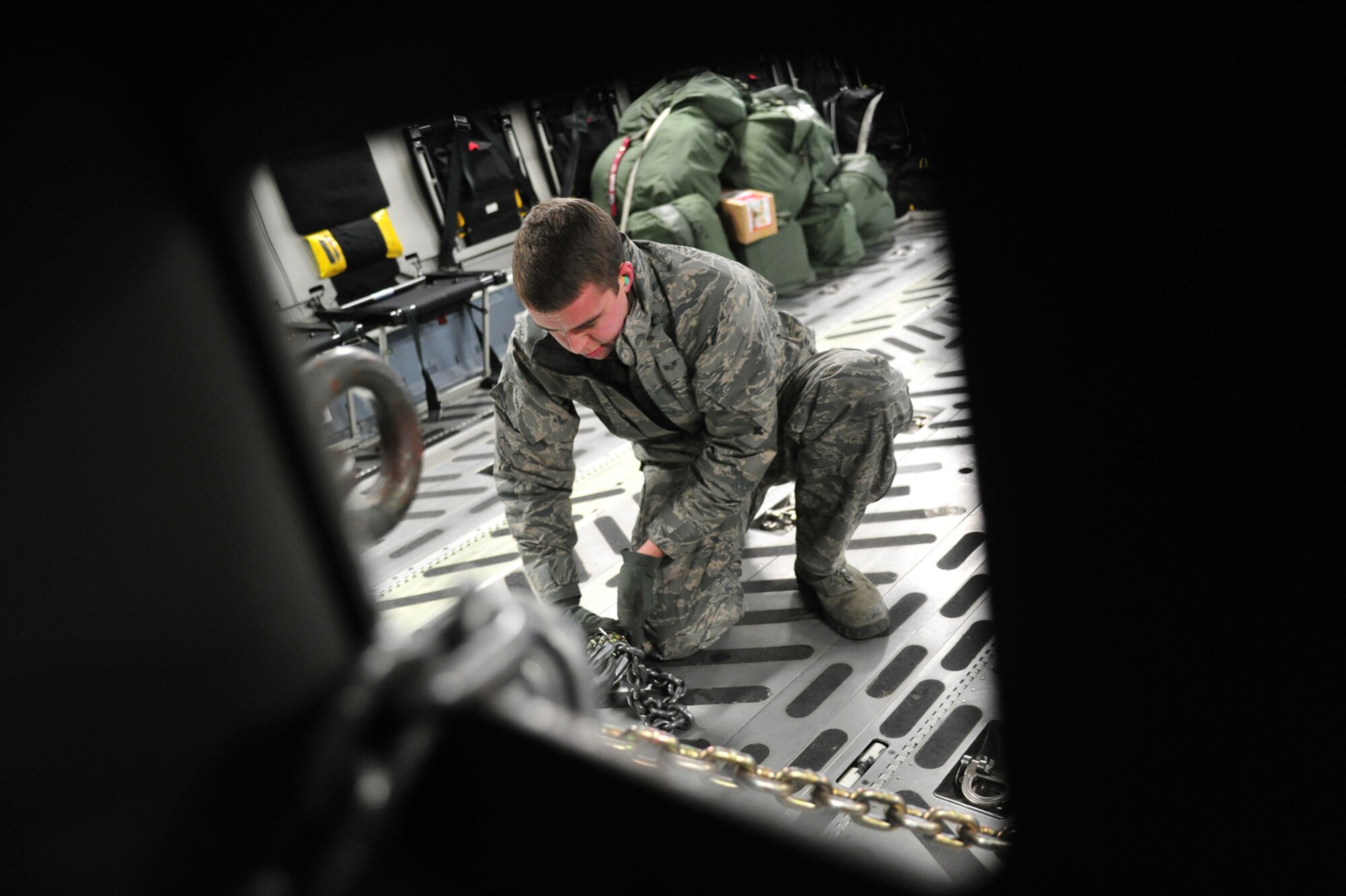 Senior Airman Lee Motz, 92nd Logistics Readiness Squadron air transportation journeyman, chains down snow blowing equipment to a C-17 Globemaster III at Fairchild Air Force Base, Wash., Dec. 4, 2013. The equipment will be delivered to the Transit Center at Manas, Kyrgyzstan, in preparation for the incoming weather. (U.S. Air Force photo by Senior Airman Taylor Curry/Released)