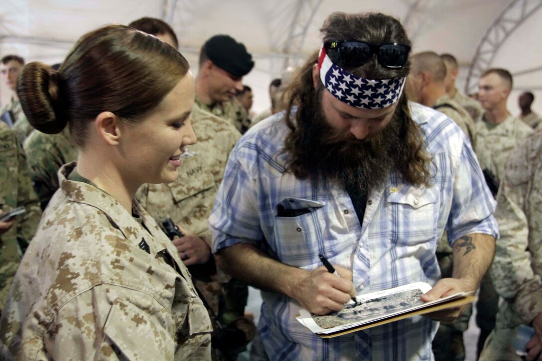 Willie Robertson, right, one of the stars of A&E's "Duck Dynasty," autographs a photo of the show's cast for U.S. Marine Sgt. Mariah Brown, during the  annual USO holiday tour on Camp Leatherneck, Afghanistan, Dec. 10, 2013. 