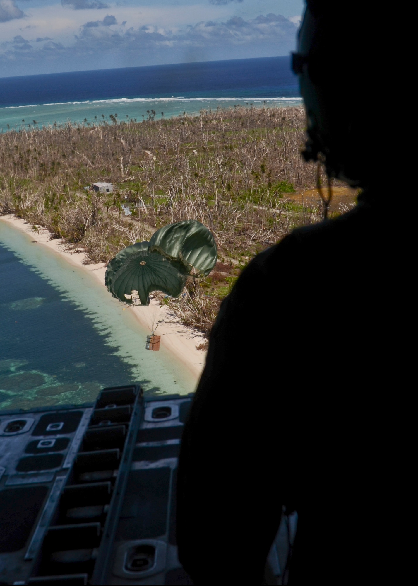 A loadmaster from the 36th Airlift Squadron from Yokota Air Base, Japan, watches as a package makes its way to the shore Kayangel Island during an Operation Christmas Drop mission over the Pacific Ocean Dec. 11, 2013. The Island of Kayangel also experienced the devastating effects of Typhoon Haiyan that ravaged the Philippines and other island in the area. (U.S. Air Force photo by Senior Airman Marianique Santos/Released)