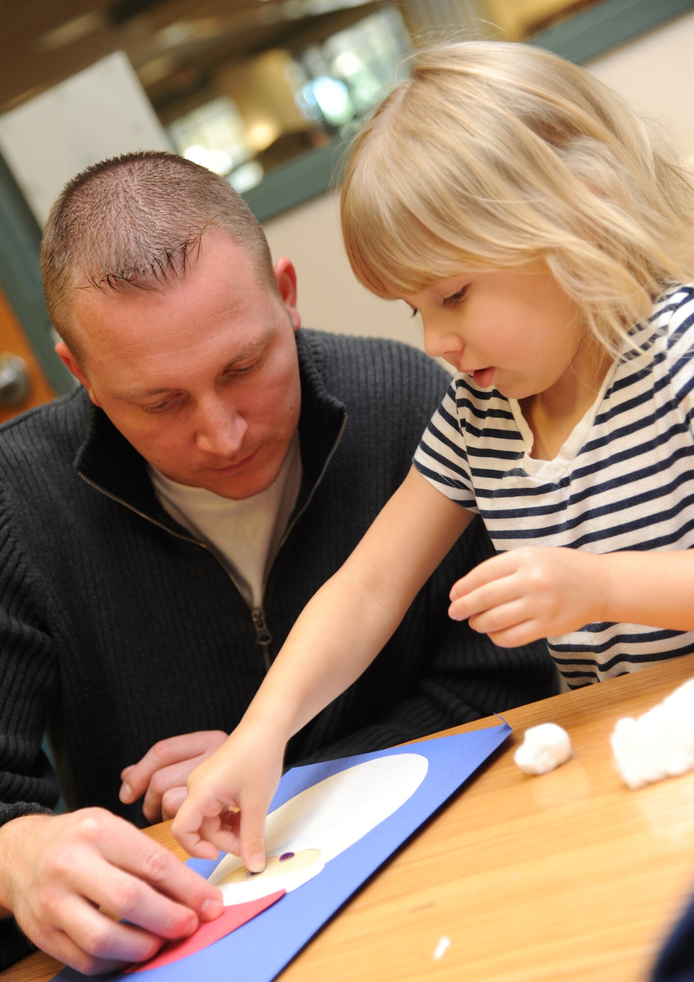 Master Sgt. Daniyel Blankenship, Keesler firefighter, assists his daughter with assembling a Santa Claus face out of construction paper and other art supplies during the McBride Library open house story time session Dec. 11, 2013, at Keesler Air Force Base, Miss.  Keesler children were also read the books “Dream Snow” and “Twas The Night Before Christmas” during story time.  (U.S. Air Force photo by Kemberly Groue)
