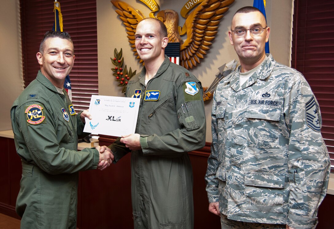 Maj. Jacob Johnson, middle, 47th Flying Training Wing wing inspection team chief, poses with Col. Brian Hastings, left, 47th FTW commander, and Chief Master Sgt. Garry Berry, right, 47th FTW command chief after being presented the XLer of the week award here Dec. 4, 2013. The XLer is a weekly award chosen by wing leadership and given to those who consistently make outstanding contributions to Laughlin and their unit. (U.S. Air Force photo/ Senior Airman John D. Partlow)