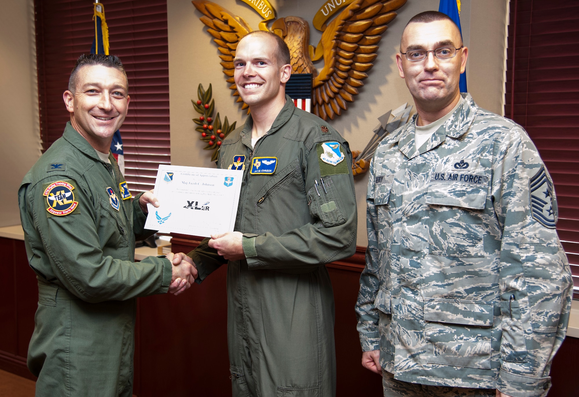 Maj. Jacob Johnson, middle, 47th Flying Training Wing wing inspection team chief, poses with Col. Brian Hastings, left, 47th FTW commander, and Chief Master Sgt. Garry Berry, right, 47th FTW command chief after being presented the XLer of the week award here Dec. 4, 2013. The XLer is a weekly award chosen by wing leadership and given to those who consistently make outstanding contributions to Laughlin and their unit. (U.S. Air Force photo/ Senior Airman John D. Partlow)