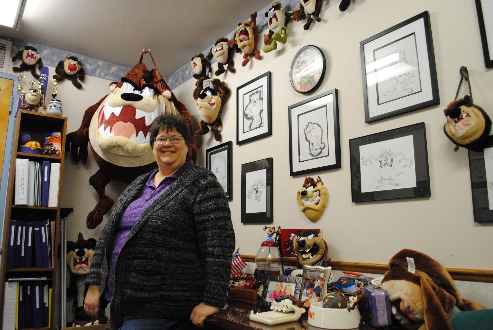Rhonda Henneman, 319th Medical Group director of housekeeping, stands by a wall decorated with various figures and drawings of Taz the Tasmanian Devil on Dec. 10, 2013, at her office inside the Medical Treatment Facility at Grand Forks Air Force Base, N.D. Henneman, the base’s Warrior of the Week for the second week of December 2013, has more than 250 items of the rambunctious Looney Tunes character. Some of the items were given to her as gifts from dozens of Airmen who’ve worked at the 319th MDG throughout her 26 years of service as an Air Force contractor. (U.S. Air Force photo/Staff Sgt. Luis Loza Gutierrez) 

