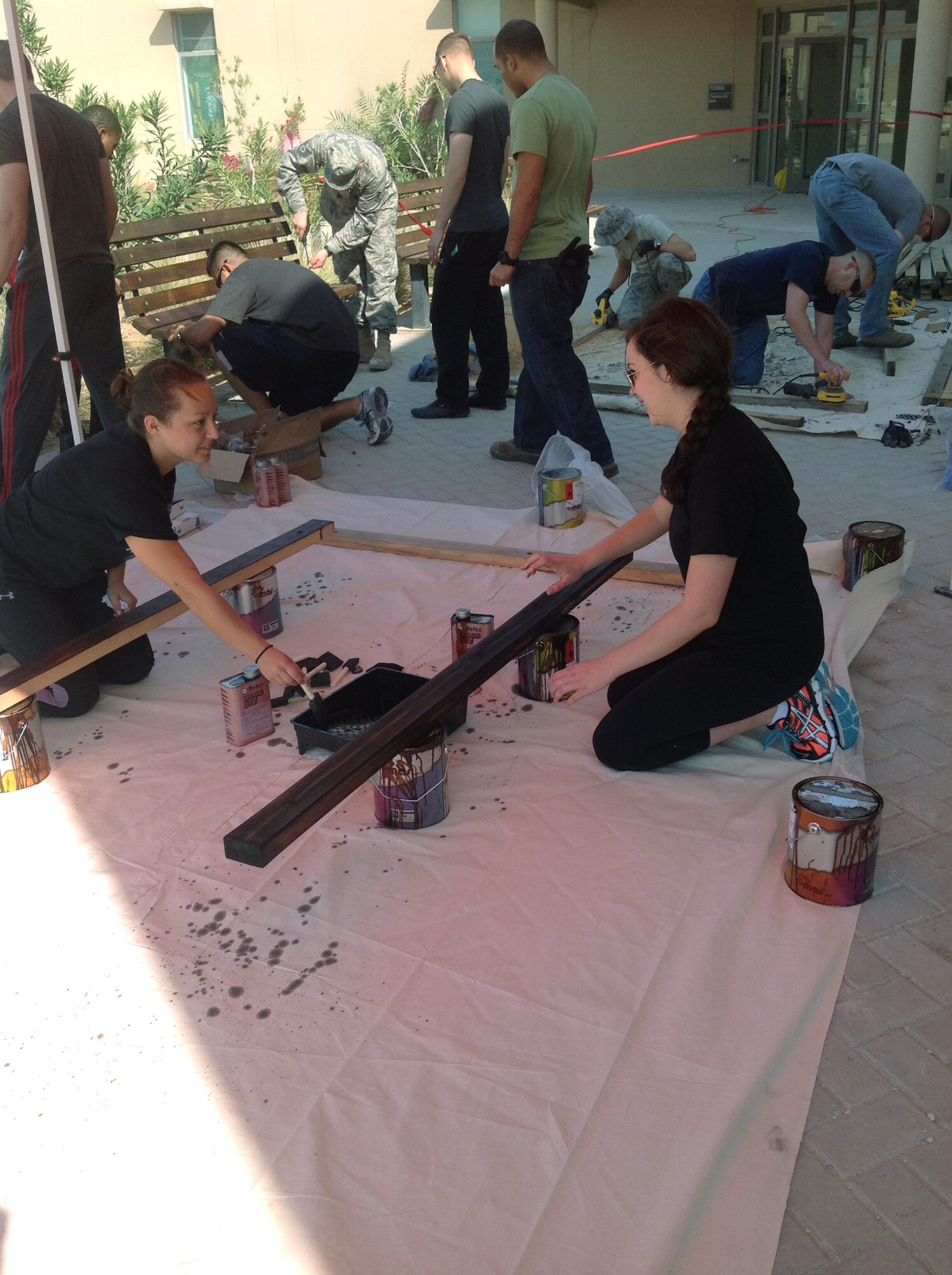Volunteers from the First Four organization refurbish and stain worn benches outside the Blatchford-Preston Complex mall. With the support of 46 Airmen and Soldiers, 16 benches were refurbished over a three day period. The mission of the First Four is to improve morale, provide welfare, and inspire growth for all individuals assigned here. (Courtesy photo)