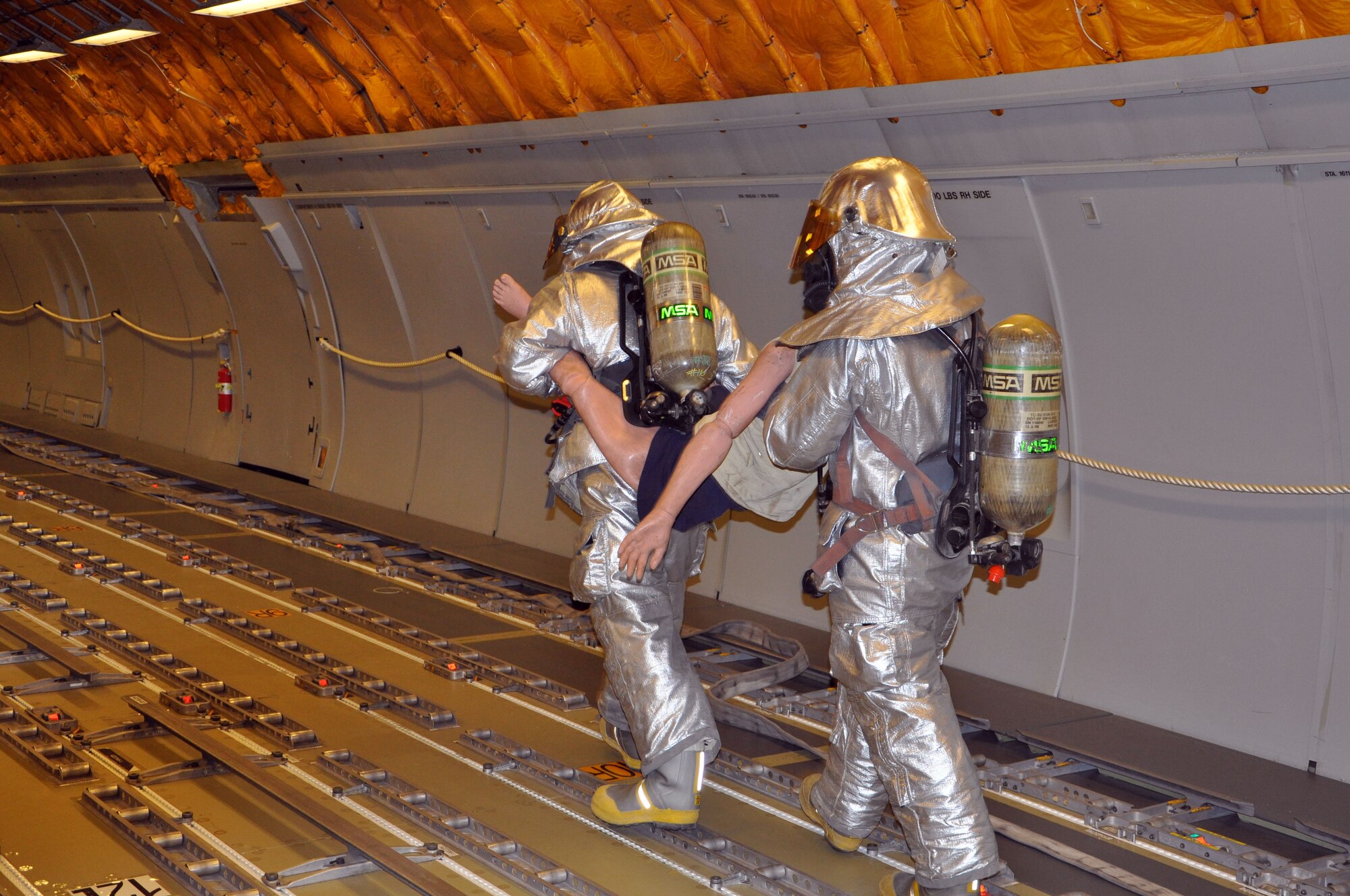 Firefighters, who are  assigned to the 380th Expeditionary Civil Engineer Squadron here, carry a training dummy to safety during a training scenario aboard a KC-10 Extender here Dec. 10, 2013. (U.S. Air Force photo by Master Sgt. April Lapetoda/Released)