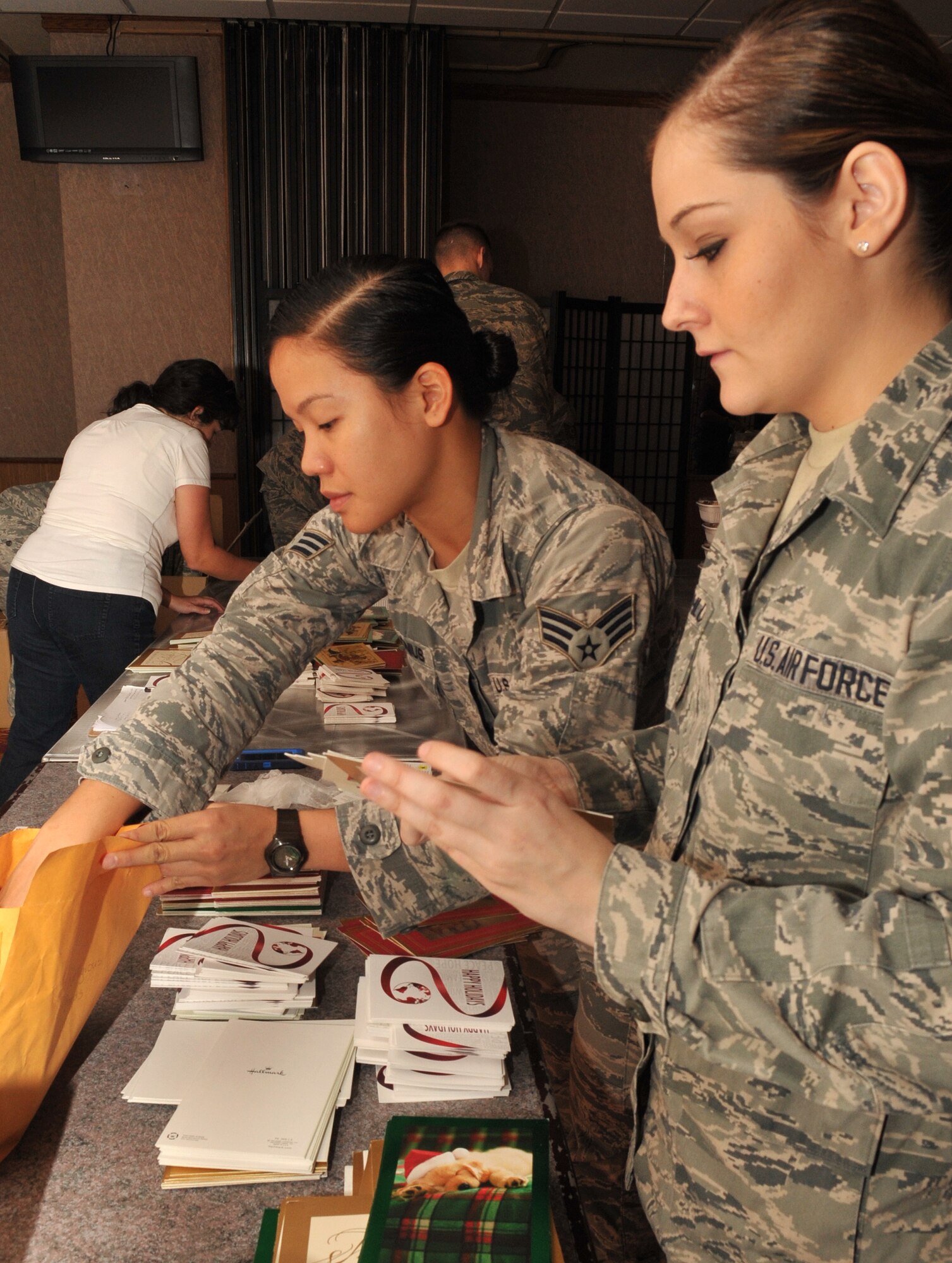 U.S. Air Force Senior Airman Amalia Personius (center), 18th Aerospace Medicine Squadron aerospace medical technician, and Airman 1st Class Carly Schlum (right), 18th Aerospace Medicine Squadron aeromedical staging technician, organizes holiday cards during the 2013 Team Kadena Cookie Drive on Kadena Air Base, Japan, Dec. 11, 2013. Personius and Schlum were among the approximately 100 volunteers to help distribute the homemade cookies to single dorm residents on the base. (U.S. Air Force photo by Naoto Anazawa)