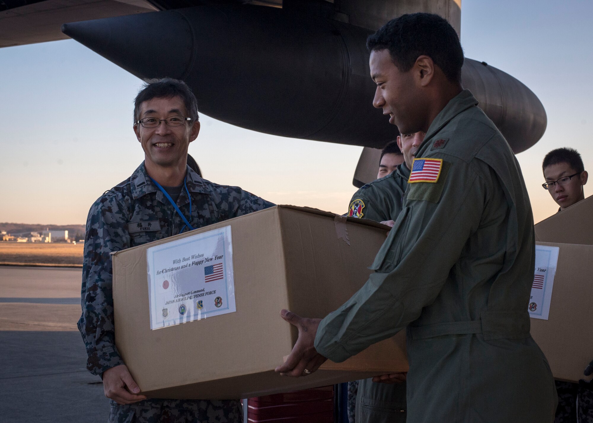 A Japanese and U.S. Airman carry a box of donated goods provided by the Japan Air Self Defense Force aboard a U.S. C-130 Hercules at Yokota Air Base, Japan, Dec. 13, 2013. The goods will be dropped over several islands in the Federated States of Micronesia as a part of Operation Christmas Drops. (U.S. Air Force photo by Captain Raymond Geoffroy/Released)