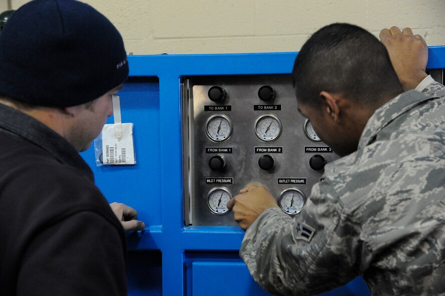 Josh Wendell, 341st Civil Engineer Squadron firefighter (left), helps Airman 1st Class Vincent Stroud, 341st CES firefighter (right), operate a Mako Air System, which is used to fill oxygen cylinders. Crews at the Malmstrom Air Force Base Fire Department operate on 24-hour shifts and must be in full gear and out the door within 60 seconds from the moment an alarm sounds. (U.S. Air Force photo/Airman 1st Class Collin Schmidt)