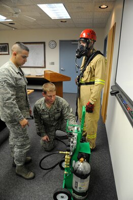 Airman 1st Class Zach Torres, 341st Civil Engineer Squadron firefighter (left), and Senior Airman Josh Grohe, 341st CES firefighter (center), operate a Supplied Air Respirator as Senior Airman Peter Kurimai, 341st CES firefighter (right), wears a firefighting uniform with an oxygen mask during  classroom training at the Malmstrom Fire Department on Dec. 5. Malmstrom firefighters perform daily classroom exercises to stay up-to-date on current safety regulations. (U.S. Air Force photo/Airman 1st Class Collin Schmidt)