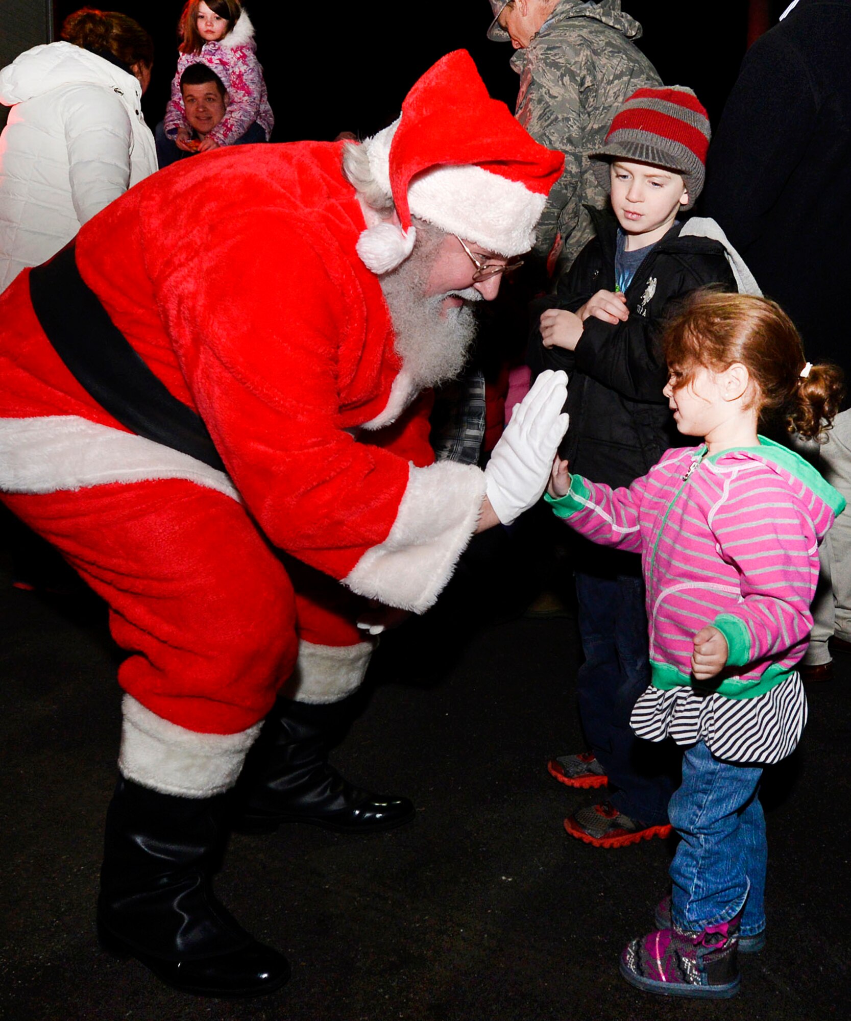 Santa Claus high-fives Kacey Belin after arriving on a fire truck to deliver candy to children and adults during the Christmas Tree Lighting ceremony at the base chapel Dec. 4 as Talmage Wright looks on. The event also included music in the Chapel sanctuary, flipping the switch outside to light the tree followed by refreshments and photos with Santa. (U.S. Air Force photo by Walter Santos)