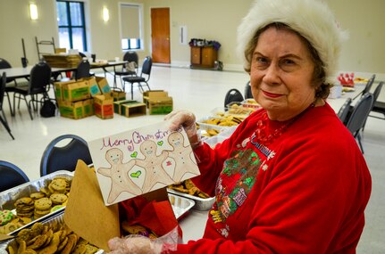 June Griggs, a member of the Team Charleston Spouses Club since 1966, holds up a card made by local school children before she adds it to a box of cookies and other edible goodies Dec.11, 2013 at the Chapel Annex on Joint Base Charleston — Air Base, S.C. The Team Charleston Spouses Club collected more than 6,500 cookies and edible goods to be distributed to deployed members Joint Base Charleston, the Gaylor Dining Facility and the Naval Weapon Station Galley. (U.S. Air Force photo/Airman 1st Class Michael Reeves)