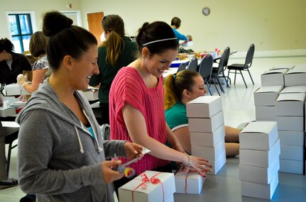 Team Charleston Spouses Club members Crystal Froehlich (left) and Amanda Roberts (center) share a laugh as they tie holiday ribbons on the boxes of cookies and edible goodies being sent to deployed Joint Base Charleston Airmen Dec.11, 2013, at the Chapel Annex on Joint Base Charleston — Air Base, S.C. The Team Charleston Spouses Club collected more than 6,500 cookies and edible goods to be distributed to deployed members Joint Base Charleston, the Gaylor Dining Facility and the Naval Weapon Station Galley. (U.S. Air Force photo/Airman 1st Class Michael Reeves)