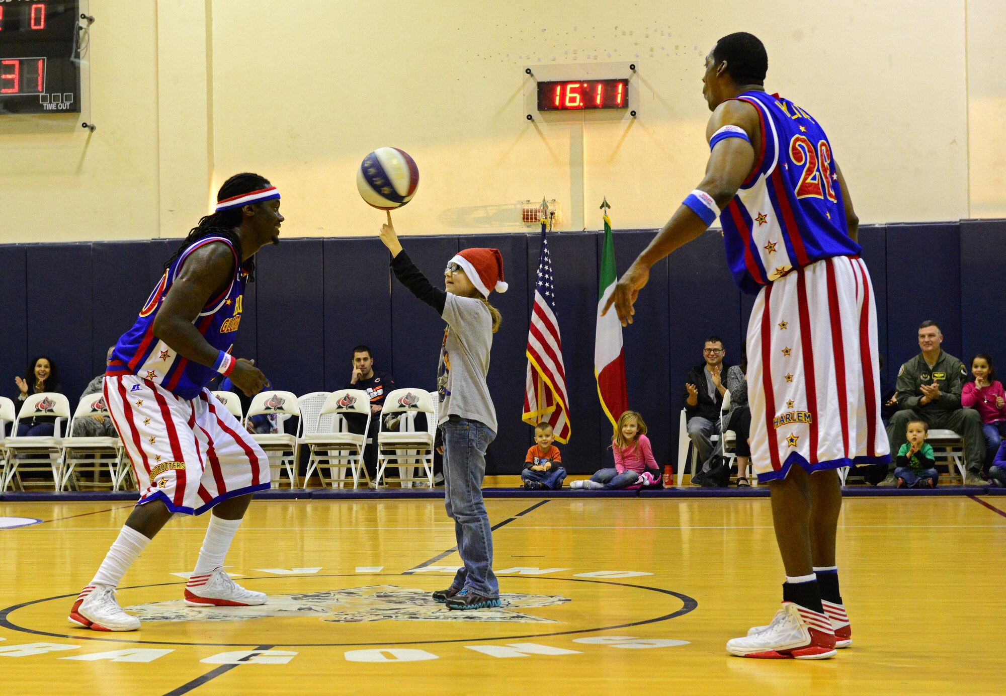 Two member of the Harlem Globetrotters watch as Eliana, age 9, daughter of Staff Sgt. Keith Broersma, 31st Civil Engineer Squadron fire inspector, spins a ball on her finger during the 12th Annual Harlem Globetrotters Holiday Tour Dec. 10, 2013, at Aviano Air Base, Italy.  Founded in 1927, the Globetrotters are an exhibition basketball team that performs around the world and combines athleticism, theater and comedy into their games. (U.S. Air Force photo/Senior Airman Michael Battles)