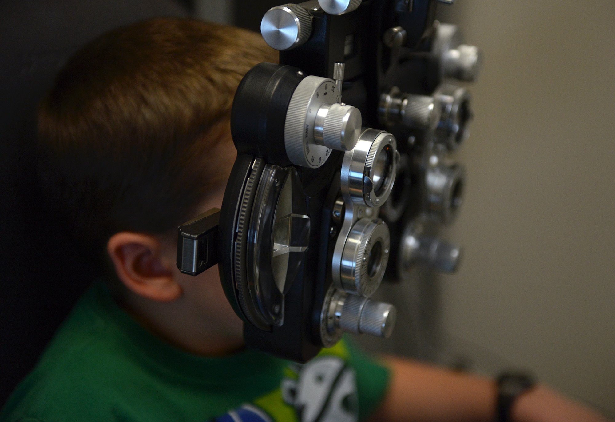 William Baker, son of Capt. Ryan Baker, reads from a vision chart at Yokota Air Base, Japan, Dec. 11, 2013. Looking through the various lenses allows the optometrists to determine whether William will require reading glasses. (U.S. Air Force photo by Airman 1st Class David Danford/Released)
