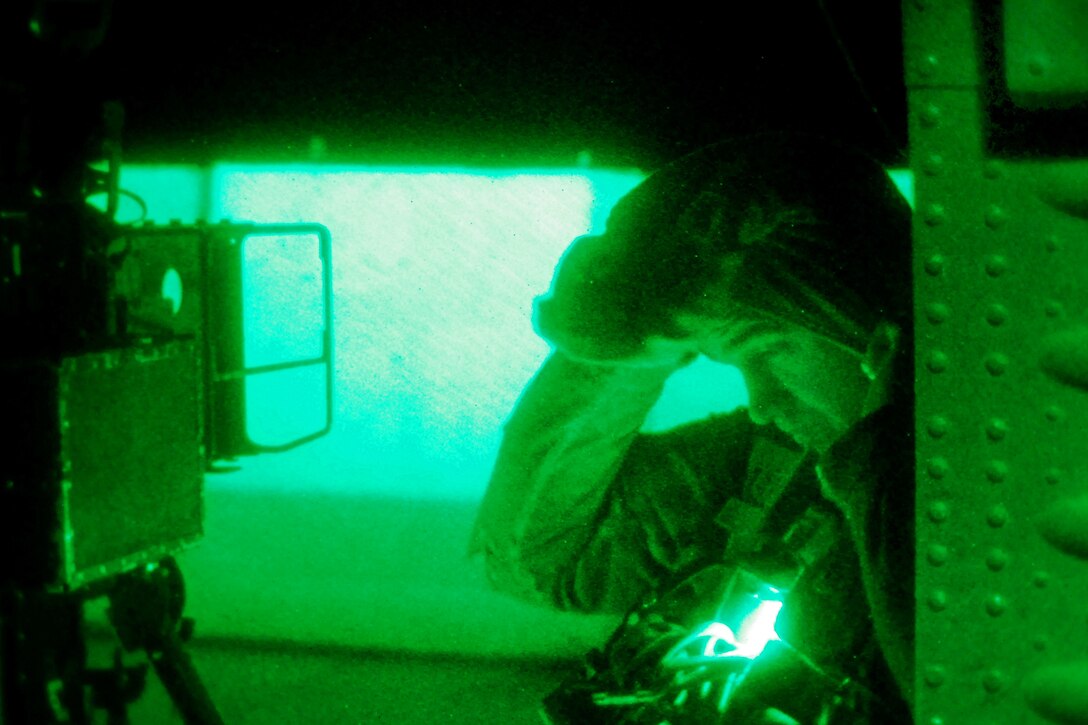As seen through a night-vision device, U.S Army Sgt. Benjamin McLaughlin puts on his cold-weather gear inside his U.S. Army UH-60M Black Hawk helicopter before a night personnel movement mission on Forward Operating Base Shank, Afghanistan, Dec. 4, 2013. McLaughlin, a crew chief, is assigned to Company C, 2nd Battalion Assault, 10th Combat Aviation Brigade.