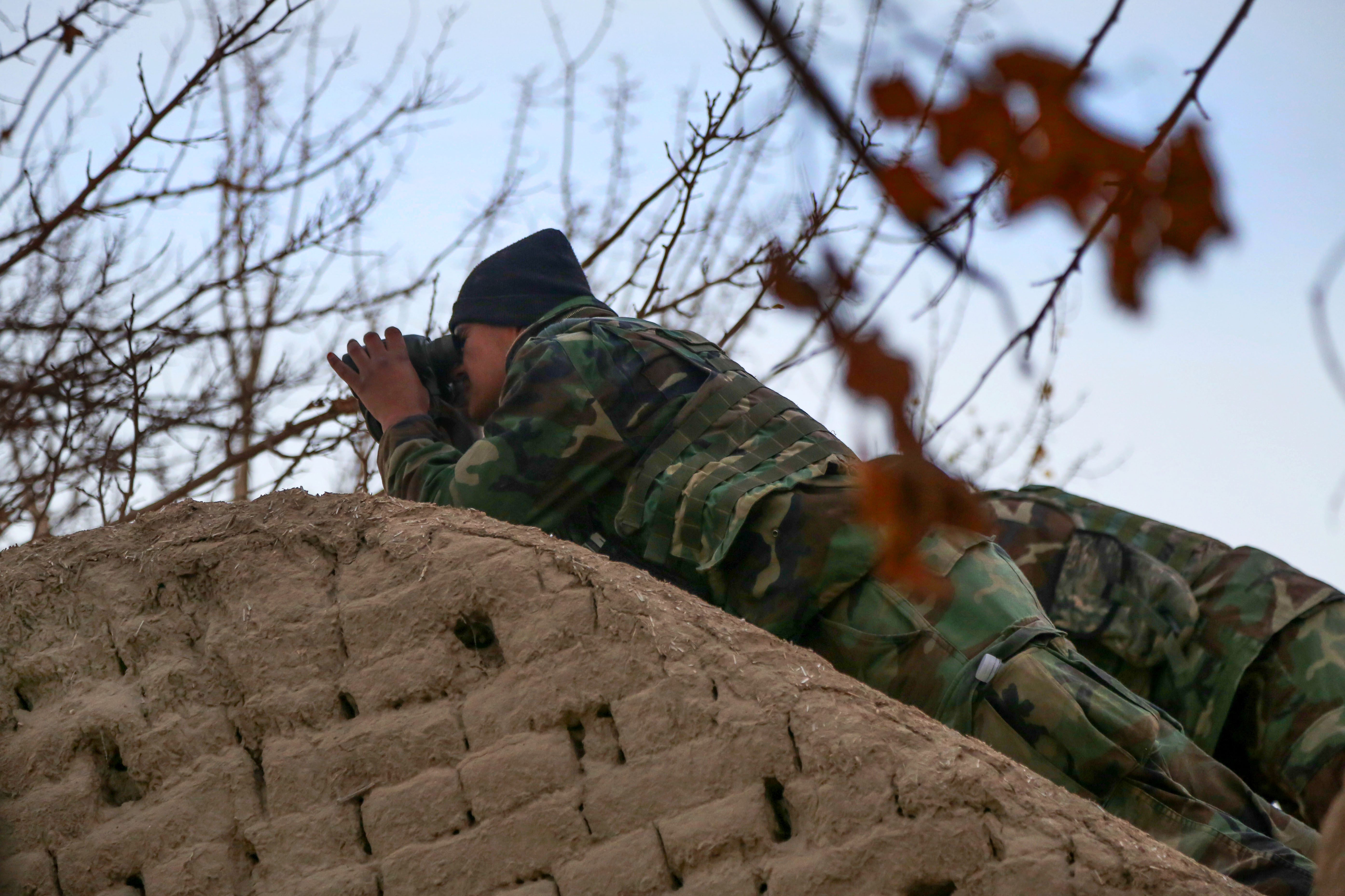 An Afghan army commando uses binoculars to scan the village of Perozi ...