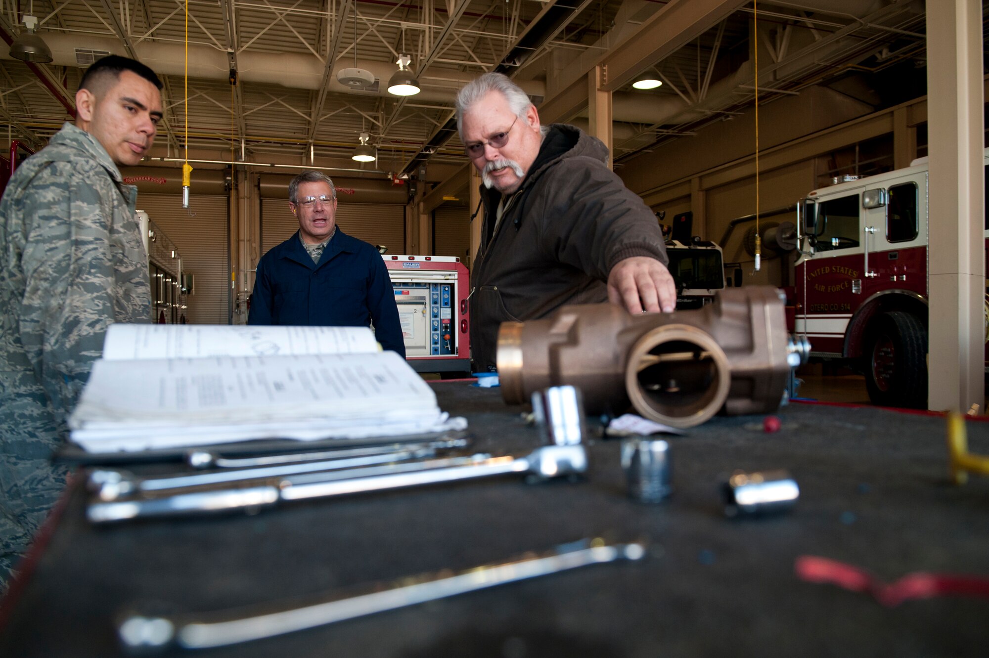 Brad Martin, fire truck mechanic and Staff Sgt. Enrique Soriano, 49th Logistics Readiness Squadron non-commissioned officer in charge of fire truck maintenance describe the process of replacing a relief valve on a P-19 fire truck to Col. Kevin Bennett, 49th Mission Support Group commander at Holloman Air Force Base, N.M., Dec. 11. Bennett spent the day working hands-on with fire truck mechanics of the 49th LRS to get an insight of their daily life and connect with the airmen. (U.S. Air Force photo by Airman 1st Class Aaron Montoya/Released)