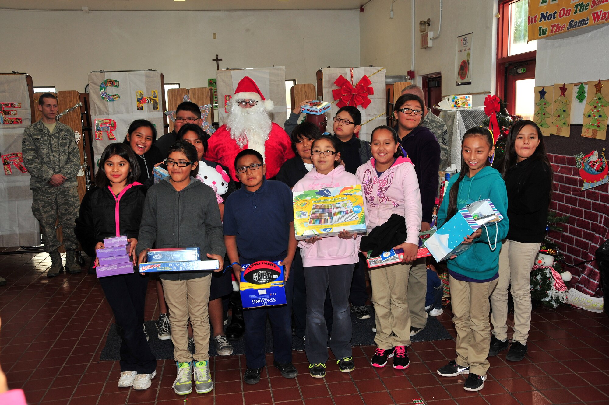 Students pose for a photo with Santa after opening their gifts at the San Xavier Mission School in Tucson, Ariz., Dec. 10, 2013. Each year Airmen and their families donate gifts to the Santas-in-Blue program and volunteers pass them out at the San Xavier Mission School . (U.S. Air Force photo by Senior Airman Josh Slavin/Released)