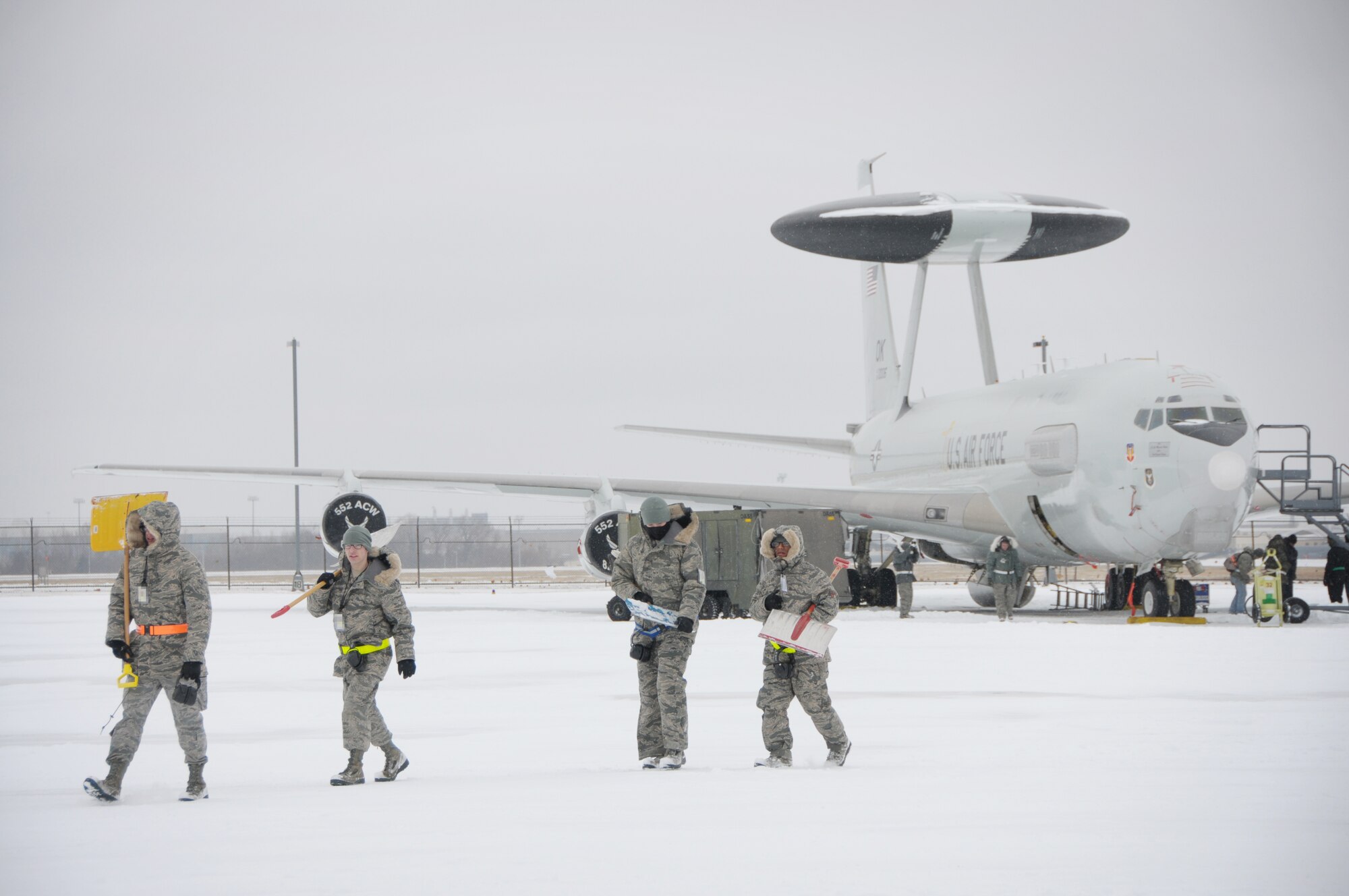Maintenance Airmen head to another E-3 Sentry after shoveling snow around the aircraft on the flight line at Tinker Air Force Base on Dec. 6. Despite the freezing temperatures and snow that have blanketed the flight line, maintainers continue to service the Airborne Warning and Control System aircraft.  (Air Force photo by Staff Sgt. Caleb Wanzer)
