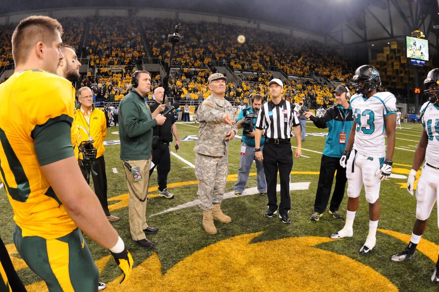 Maj. Gen. David Sprynczynatyk, North Dakota adjutant general, center, flips the coin at midfield for the North Dakota State University Bison versus Coastal Carolina University FCS quarterfinal playoff football game at the FargoDome, Fargo, N.D., Dec. 14, 2013. Sprynczynatyk is an alumnus of North Dakota State University. He earned a bachelor's degree in civil engineering in 1972, and is flipping the coin to determine who receives the ball for the opening kick-off.  The Bison won the game 48-14.