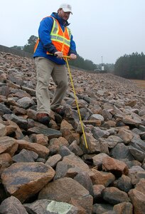 Wilmington District civil engineer Zack Nichols uses a probe to check the soil surface under a layer of riprap for any signs of erosion during the annual dam safety inspection at Falls Dam in Raleigh. (USACE photo by Hank Heusinkveld)