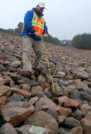 Wilmington District civil engineer Zack Nichols uses a probe to check the soil surface under a layer of riprap for any signs of erosion during the annual dam safety inspection at Falls Dam in Raleigh. (USACE photo by Hank Heusinkveld)