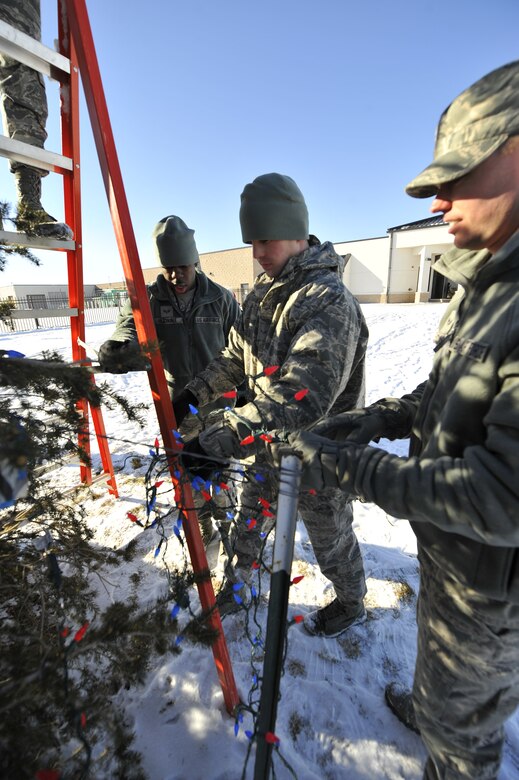Senior Airman Wendell Hudnall Jr., 460th Space Communications Squadron, left; Airman 1st Class Brandon Maun, 460th SCS, center; and Senior Airman Ryan Clancey, 460th SCS, string lights across a Christmas tree, Dec. 9, 2013, on Buckley Air Force Base, Colo. The tree was lit in memory of Kristopher Mansfield, a former 460th SCS Airman who was killed by a drunk driver. Friends and family decorate the tree in celebration of Mansfield’s life and what he meant to the squadron. (U.S. Air Force photo by Airman 1st Class Samantha Saulsbury/Released)