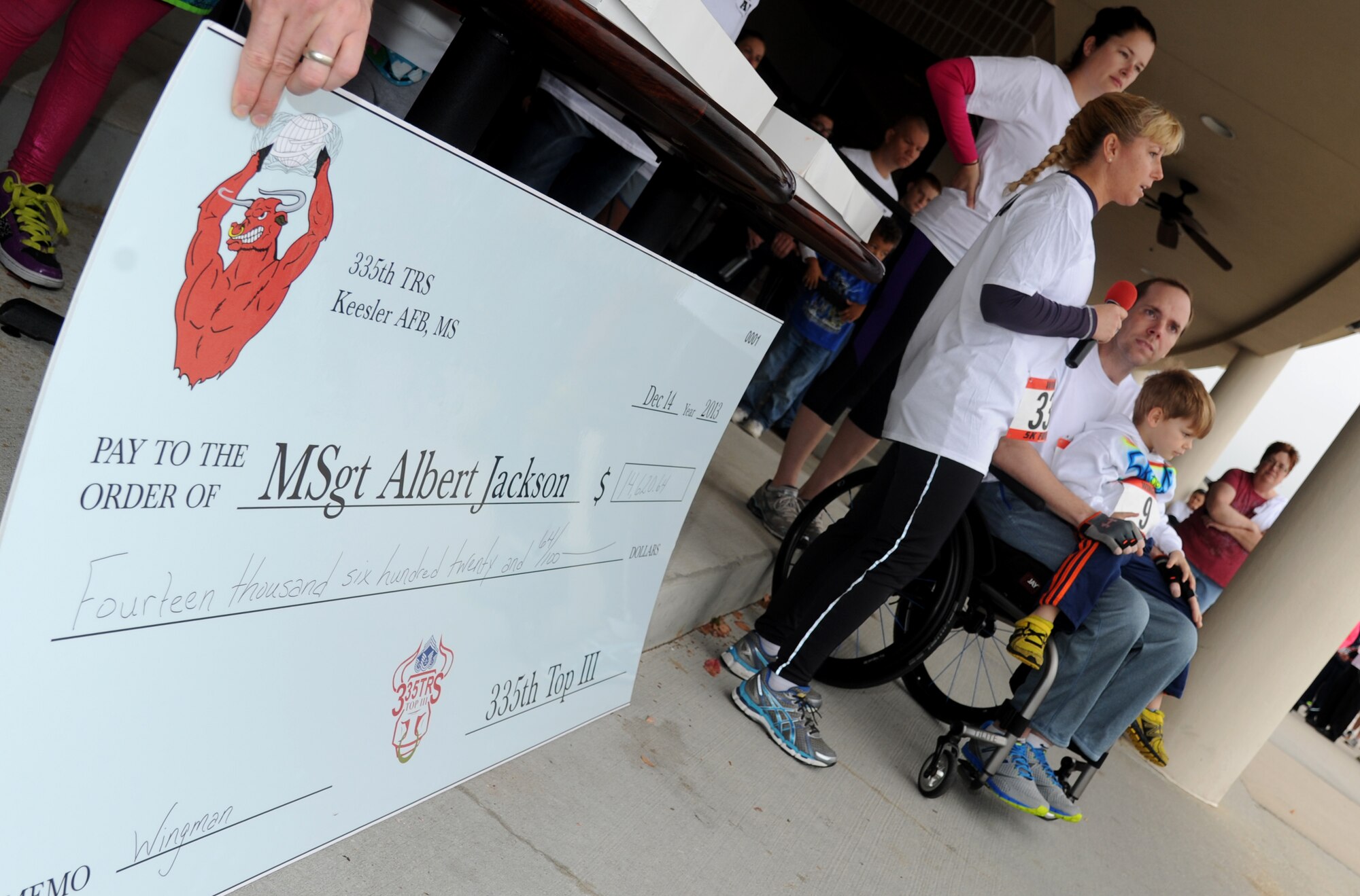 A check in the amount of $14,620.64 stands on display as Lt. Col. Betsy Ross, 335th Training Wing commander, addresses the crowd on their donations during the “5K for AJ” benefit run Dec. 14, 2013, Keesler Air Force Base, Miss. The 5K run was held to raise money for Master Sgt. Albert “AJ” Jackson, 335th TRS, who was paralyzed from a medical procedure. The event, organized by the 335th TRS “Bulls,” raised more than $15,700 to assist the family.  (U.S. Air Force photo by Kemberly Groue)