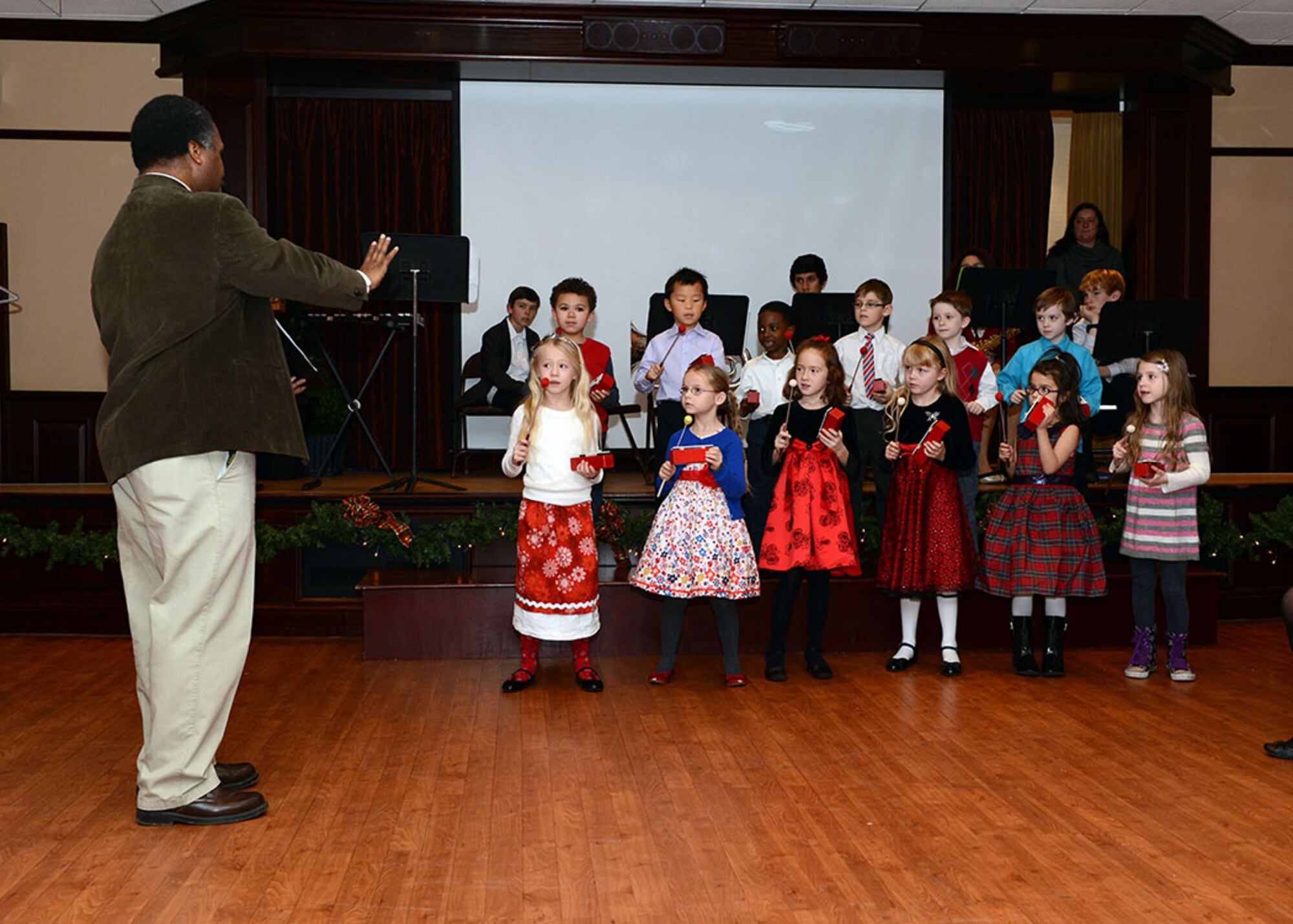 RAF MENWITH HILL, United Kingdom - John Cooper, Menwith Hill School band director, leads the first grade class in a song on the bells during the RAF Menwith Hill Tree Lighting ceremony at the community club Dec. 5. Students from the MHS School provided entertainment for the community by singing carols and playing holiday music while children in the School Aged Program performed a skit and led the audience in a silly Christmas sing-along. (U.S. Air Force photo by Staff Sgt. Debbie Lockhart)