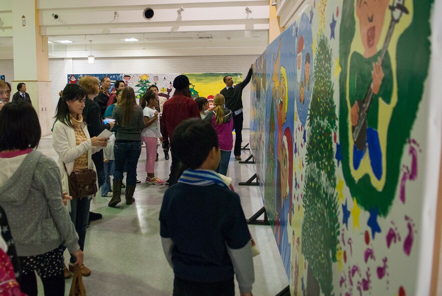Children and adults view holiday artwork Dec. 14, 2013, at the Korinza Shopping Mall in Okinawa City, Japan. The art is for the 2013 Okinawa City Japan-US Kids Holiday Art Fest where 12 groups of children from Kadena, Bob Hope, and Stearley Heights Elementary Schools, Amelia Earhart Intermediate School, and Okinawa City  schools painted holiday-themed murals. The event is a collaboration between Kadena Top 3's Okinawa Outreach, a group focused on strengthening relationships between local Okinawans and armed forces members and their families, 18th Wing Public Affairs community relations, and the non-profit organization Beautiful Community Project Network. The murals are on display on Park Avenue outside Gate 2 until Dec. 28. The murals are scheduled to be voted on during a ceremony on Park Avenue from noon until 3:30 p.m. on Dec. 22, then the winners will be announced from 4 to 5 p.m.