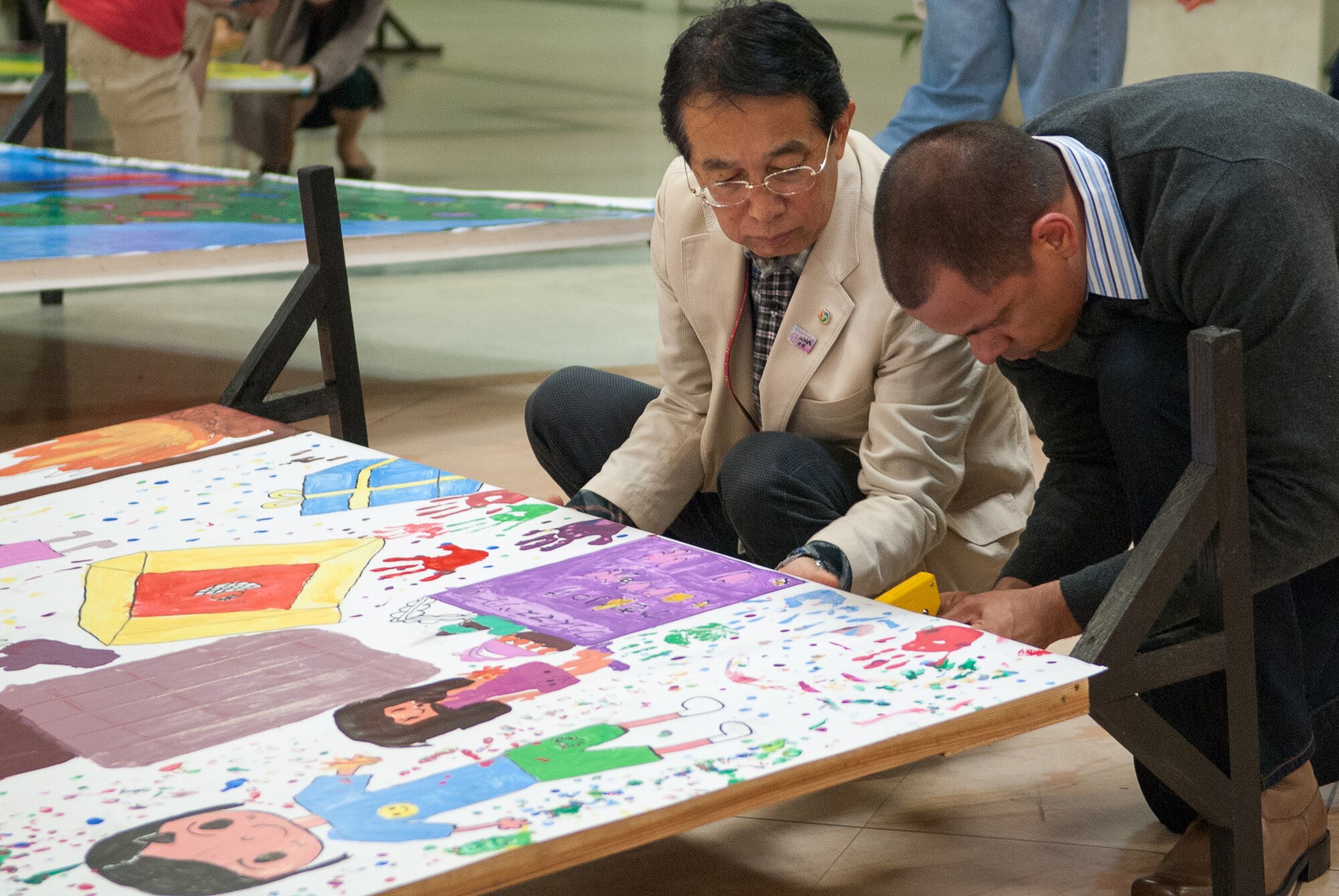 Tech. Sgt. Steven Whitley, 18th Maintenance Operations Squadron NCO in charge of maintenance management analysis, and Nobuo Higa, president of the non-profit organization Beautiful Community Project Network, secure children's artwork to display boards Dec. 14, 2013, at the Korinza Shopping Mall in Okinawa City, Japan. The art is for the 2013 Okinawa City Japan-US Kids Holiday Art Fest where 12 groups of children from Kadena, Bob Hope, and Stearley Heights Elementary Schools, Amelia Earhart Intermediate School, and Okinawa City schools painted holiday-themed murals. The murals are on display on Park Avenue outside Gate 2 until Dec. 28. The murals are scheduled to be voted on during a ceremony on Park Avenue from noon until 3:30 p.m. on Dec. 22, then the winners will be announced from 4 to 5 p.m.