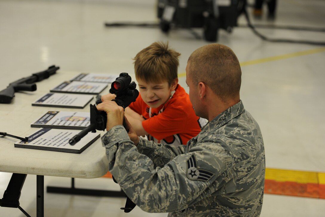 Senior Airman Matthew Caudill, 11th Wing Security Support Squadron combat arms instructor, assists Zachary Balog, 6, son of Col. Daniel Balog, stationed at the Uniformed Services University, in getting a good sight picture on an M4 rifle Dec. 14, 2013, at the 26th Annual Parents and Children Fighting Cancer Christmas Party held in Hangar 3 on Joint Base Andrews, Md. This event allows PCFC families to spend the day in a winter wonderland offering food, entertainment, gifts, static displays, and a visit from Santa and Mrs. Claus. (U.S. Air Force photo/Aimee Fujikawa)