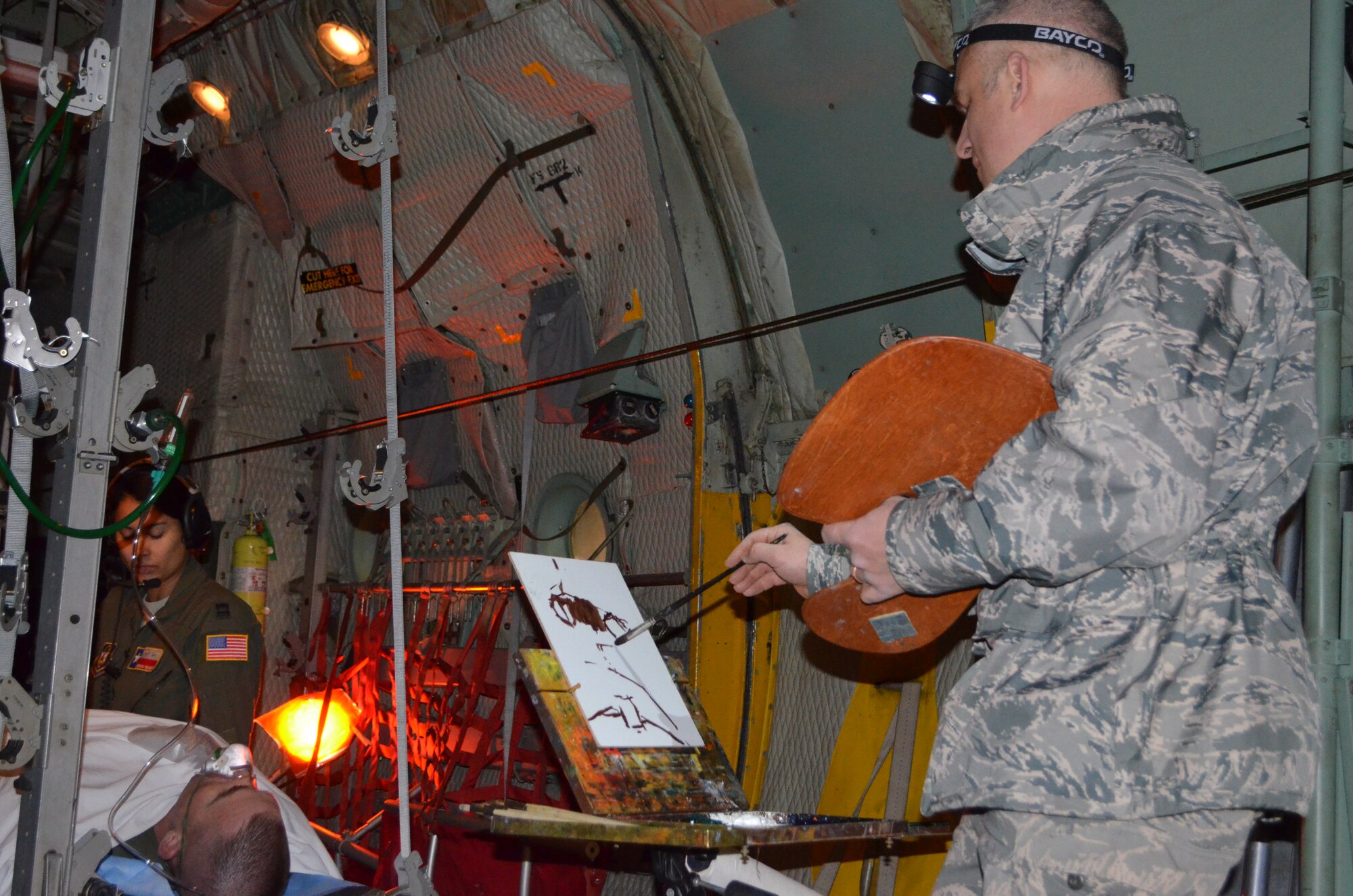 Maj. Warren Neary from tAir Force Space Command uses a pochade box to recreate the scene of Capt. Adriana Valadez, 433rd Aeromedical Squadron, Joint Base San Antonio-Lackland,Texas, aboard a C-130, the same type of aircraft that carried wounded Airman, Tech. Sgt. Zach Rhyner from Kandahar to Mazar-e Sharif, Afghanistan. Pictured, (left) SSgt Amanda Pena, who was also part of the crew, an unidentified loadmaster from the 68th Airlift Squadron on a litter, who portrays Rhyner, and Valadez on the right. All Airmen are based at Joint Base San Antonio-Lackland. (U.S. Air Force photo/1st. Lt. Cresencio Medina) 

