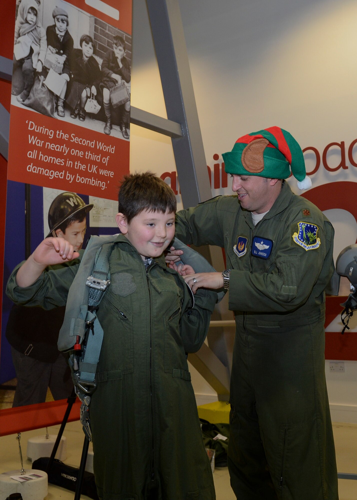 Maj. Bill Johnson, 492nd Fighter Squadron assistant director of operations, helps William Chapman, 9, into a junior flight suit during the Duxford Christmas party at the Imperial War Museum Dec. 14, 2013. Established during World War II, the Duxford Christmas party was created by the Royal Air Force Duxford 78th Fighter Group to supply gifts and support to children from the London area who were orphaned by the war. (U.S Air Force photo by Airman 1st Class Nigel Sandridge/ Released)