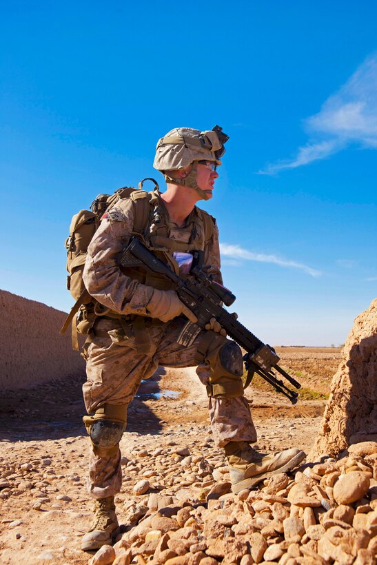 U.S. Marine Corps Lance Cpl. Ian Forry crouches behind a wall during a firefight with insurgents near a bazaar in the Nad Ali district of Afghanistan's Helmand province, Dec. 4, 2013. Forry, a rifleman, is assigned to the 1st Battalion, 9th Marines.