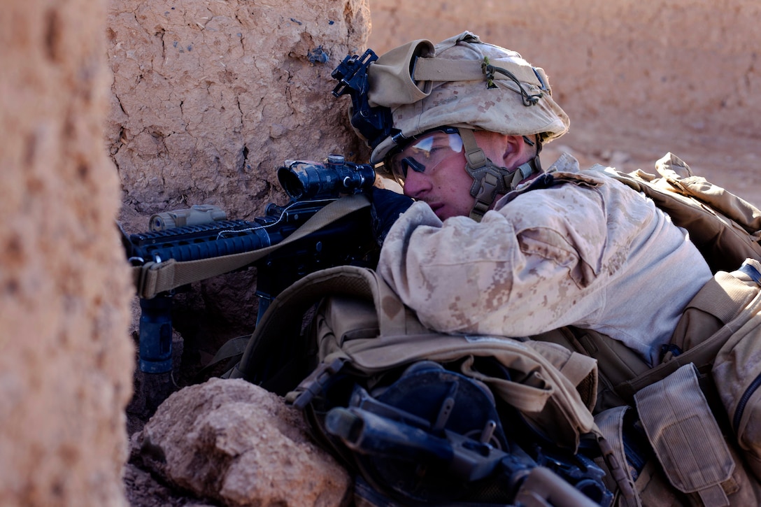U.S. Marine Corps Lance Cpl. Nathan Gulbronson provides cover fire for a group of Marines through a hole in a desert compound wall during a firefight with insurgents near a bazaar in the Nad Ali district of Afghanistan's Helmand province, Dec. 4, 2013. Gulbronson, a rifleman, is assigned to the 1st Battalion, 9th Marines.