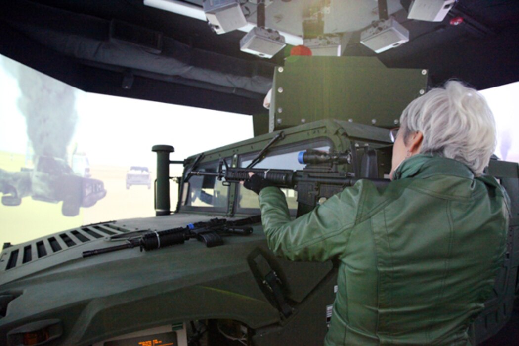 A tour participant takes aim at simulated targets on the 360-degree video screen in the combat convoy simulator at Camp Wilson.