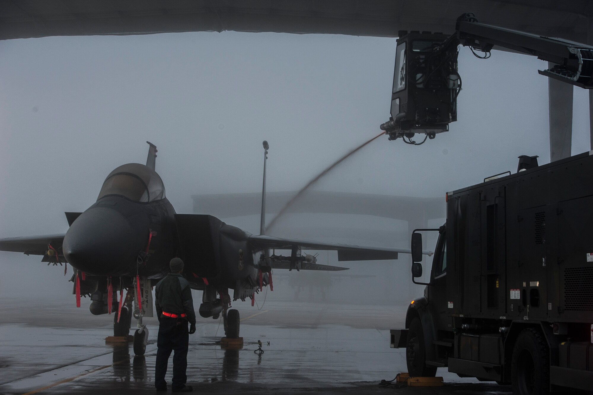 Air Force Senior Airman Brian Radtka, 366th Aircraft Maintenance Squadron crew chief, observes as Senior Airman Blake Pullen de-ices an F-15E Strike Eagle at Mountain Home Air Force Base, Idaho, Dec. 18, 2013. Preventing a build-up of snow and ice on the wings and tail is crucial for safe takeoff, and without crew chiefs and de-icing, the Mountain Home AFB fleet could literally be grounded during frigid Idaho winter months. (U.S. Air Force photo by Master Sgt. Kevin Wallace/RELEASED)