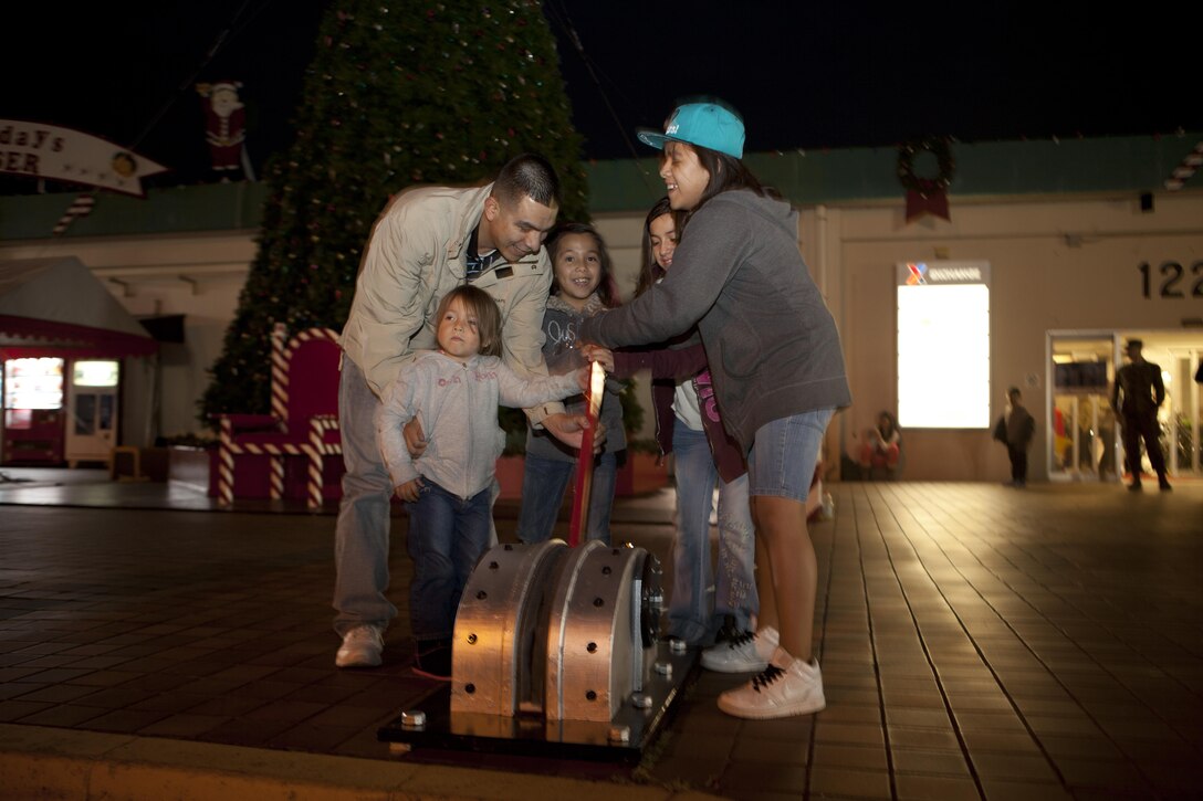 Gunnery Sgt. Cresencio Ocampo and his family pull the lever to light the Christmas tree during a ceremony Dec. 6 at the Camp Kinser Main Exchange. “Each year, we choose a Marine or sailor who has recently returned from deployment and their family to help light the tree,” said Ronald Davis, the announcer for the event. “This year, the honor goes to Gunnery Sgt. Ocampo and his family. Gunnery Sgt. Ocampo just came back from deployment, and we’re glad to have him back, safely with his family.” Ocampo is a distribution management specialist with Combat Logistics Regiment 35, 3rd Marine Logistics Group, III Marine Expeditionary Force. 