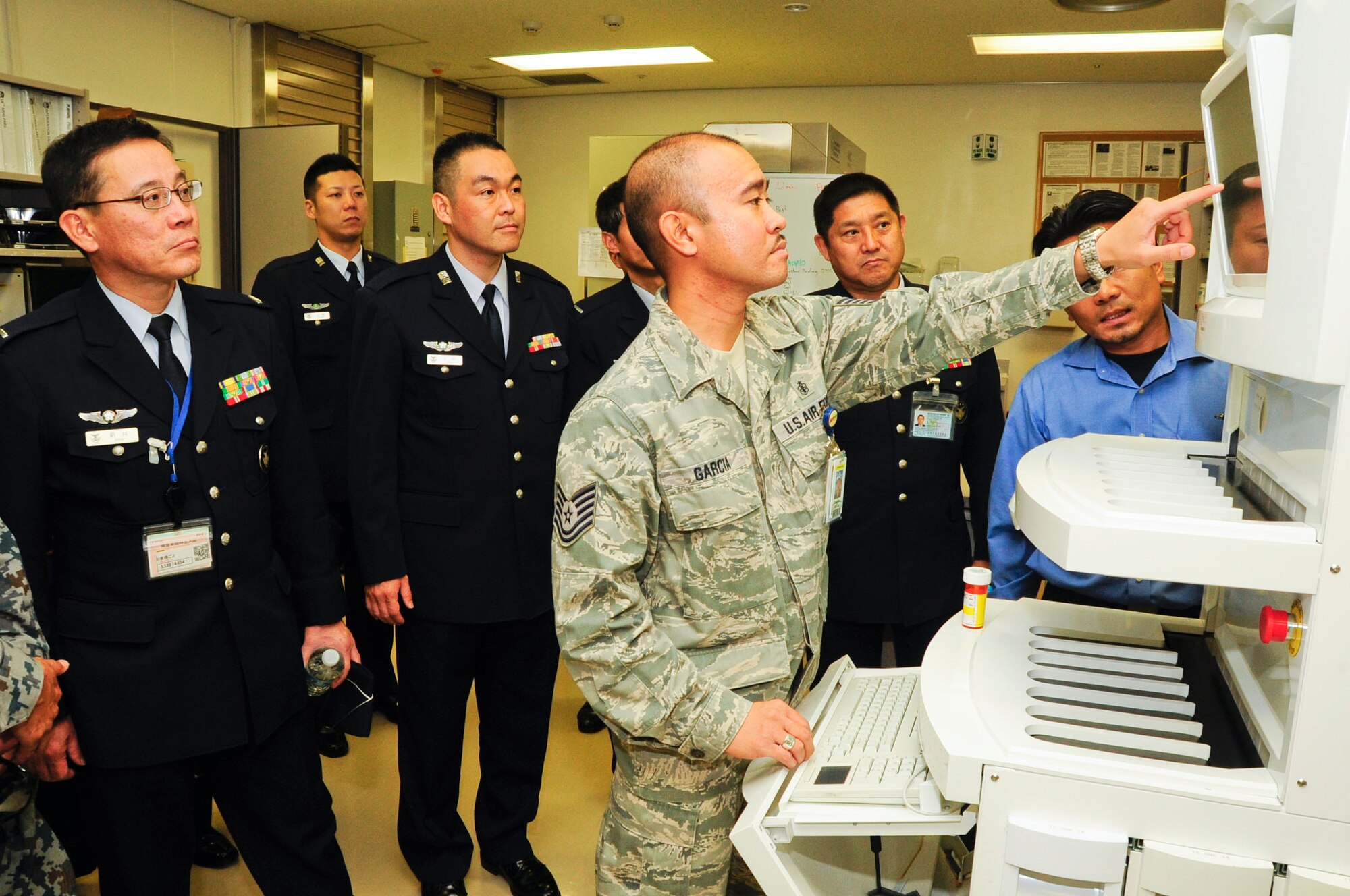 Tech. Sgt. John Garcia, 18th Medical Support Squadron pharmacy technician, shows Warrant Officer Takeshi Arai, Japan Air Self Defense Force senior enlisted advisor, the pharmacist robot during his visit to Kadena Air Base, Japan, Dec. 19. JASDF senior enlisted members toured four 18th Medical Group facilities. (U.S. Air Force photo by Staff Sgt. Darnell T. Cannady)