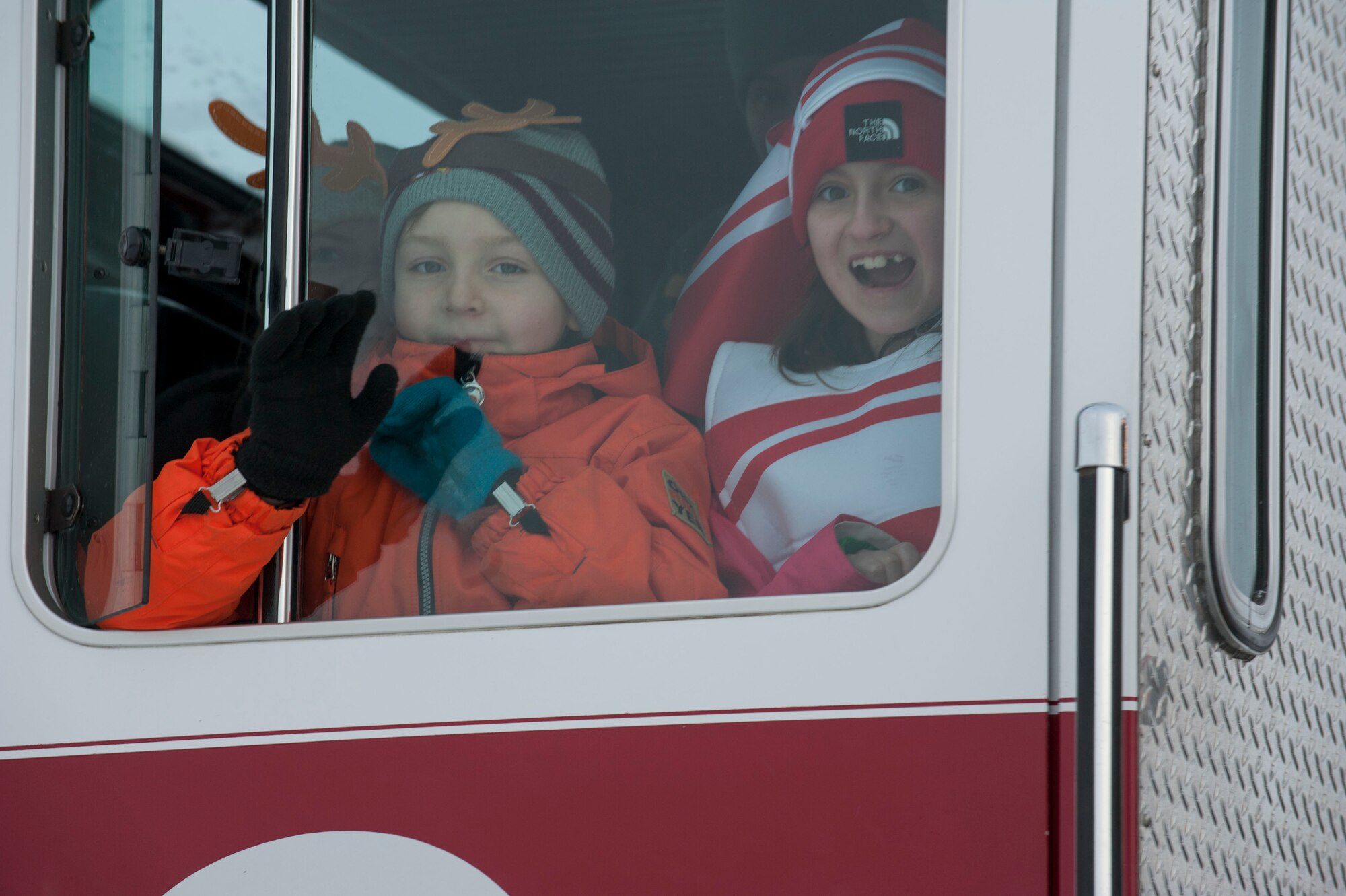 Young children wave to onlookers from inside a fire truck during the holiday parade at Minot Air Force Base, N.D., Dec. 13. The parade was organized by Balfour Beatty Communities and wound through housing for nearly one hour playing Christmas music and passing out candy to waiting children. (U.S. Air Force photo/Senior Airman Stephanie Sauberan)